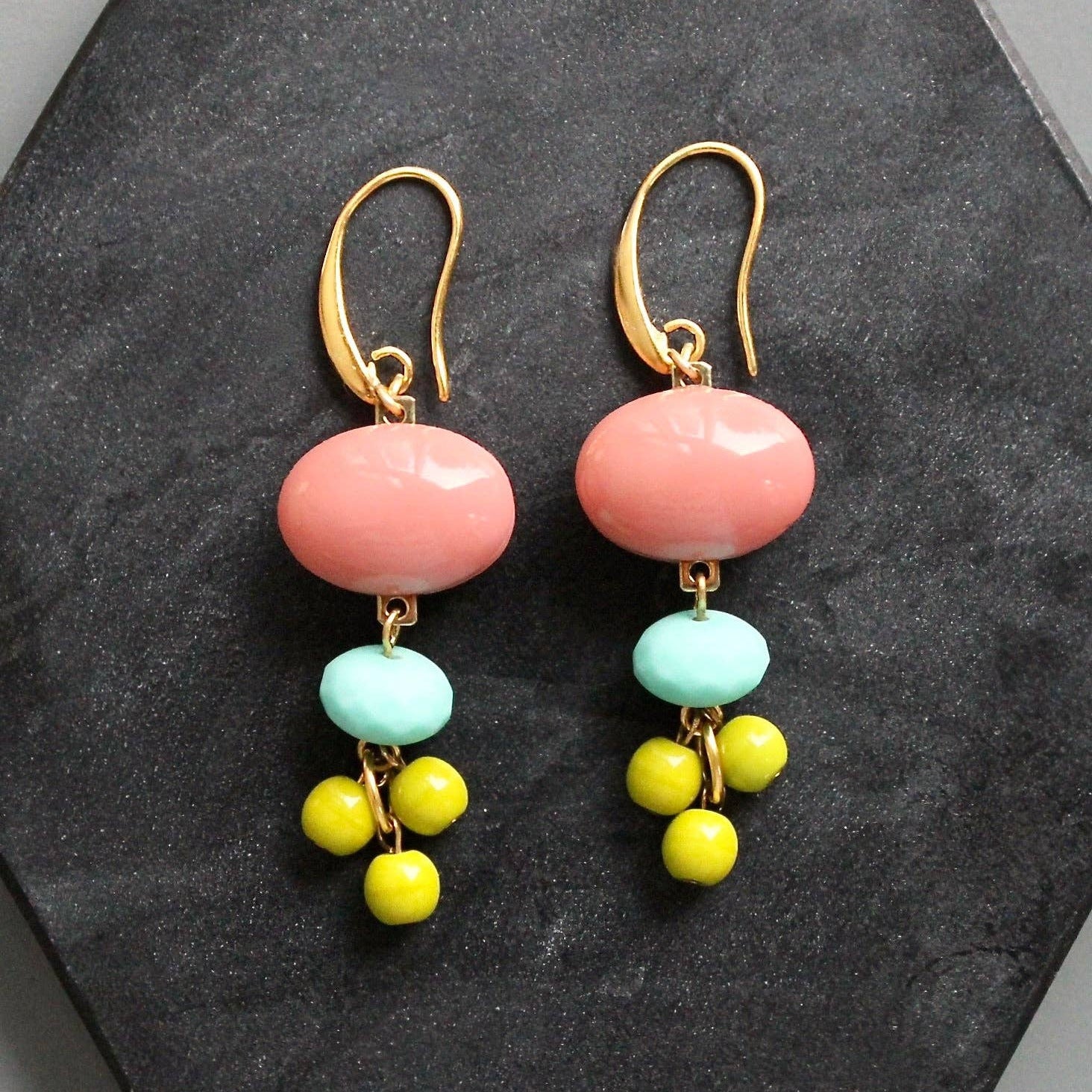 Pair of earrings with pink, turquoise, and yellow beads on a dark gray surface.