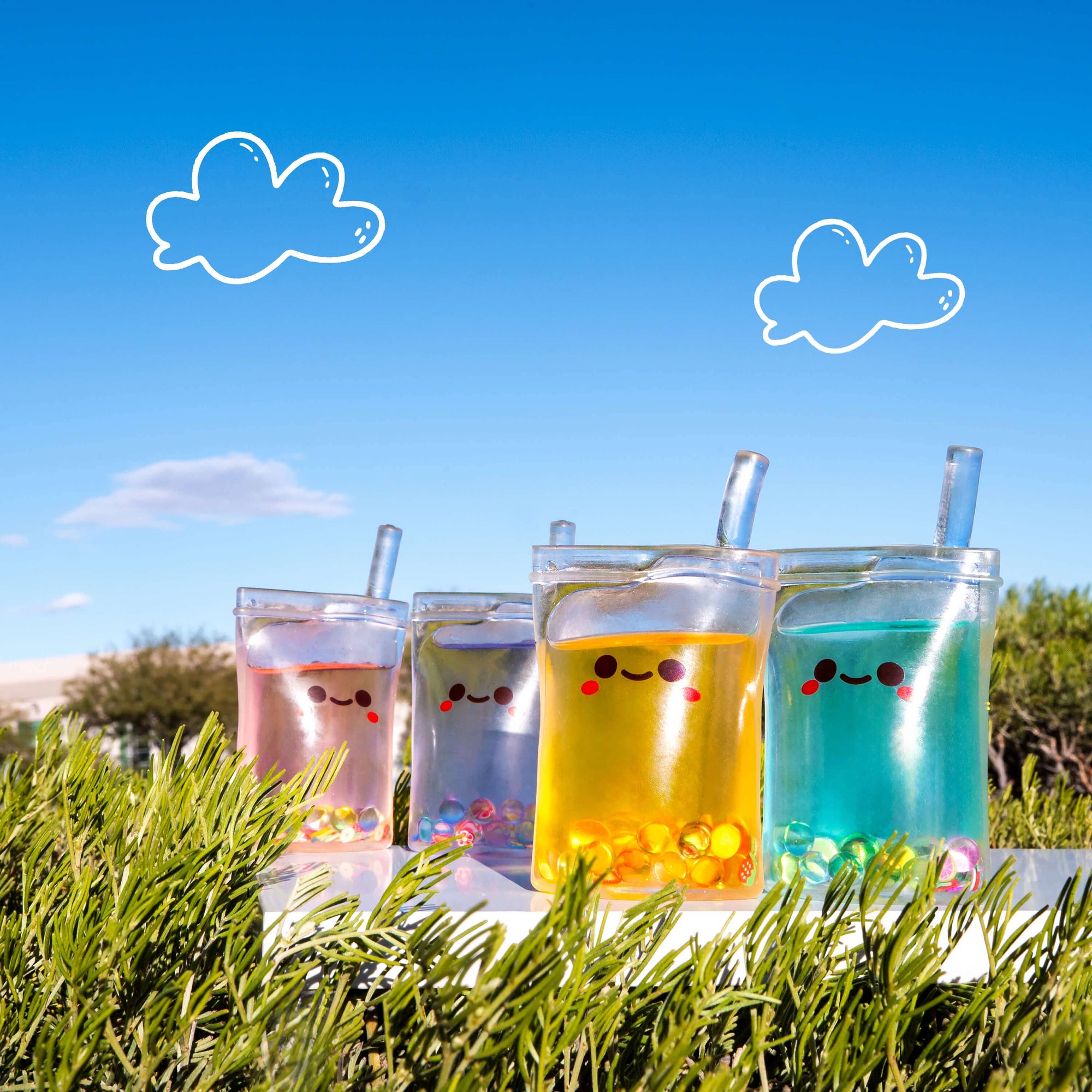 Four colorful cups with smiling faces on a grassy area with a blue sky.