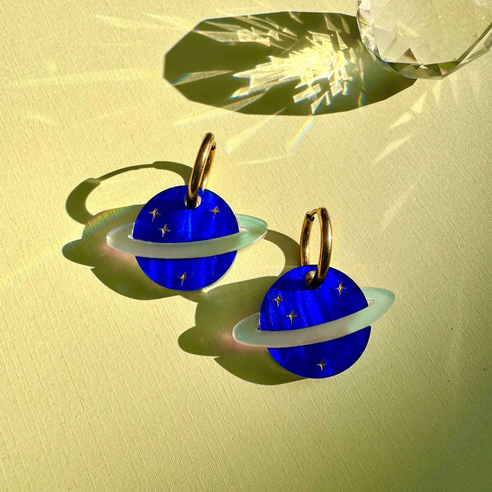 Blue planet-shaped earrings with gold accents on a yellow background