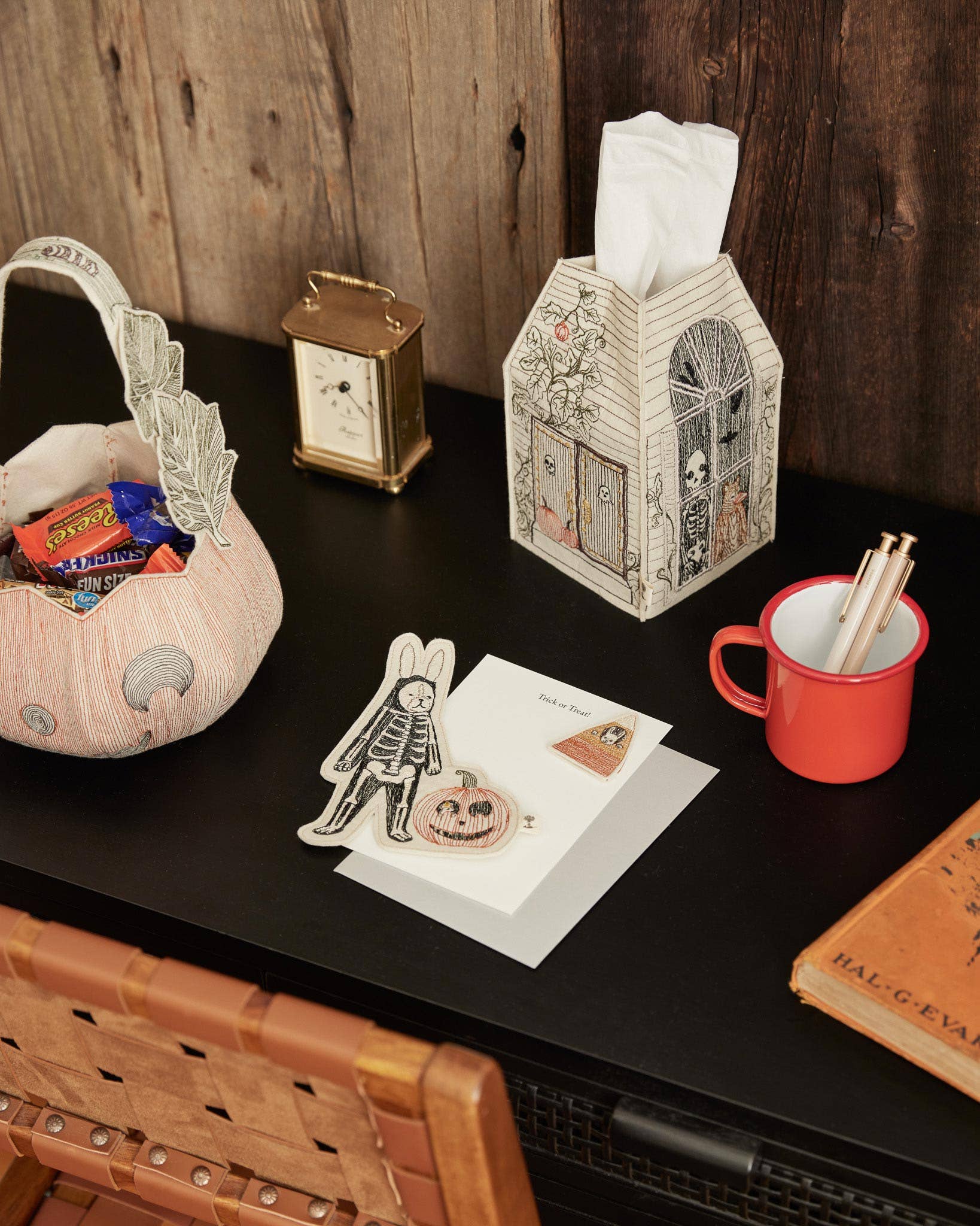 Desk with Halloween-themed items including a basket, mug, and cards against a wooden background.