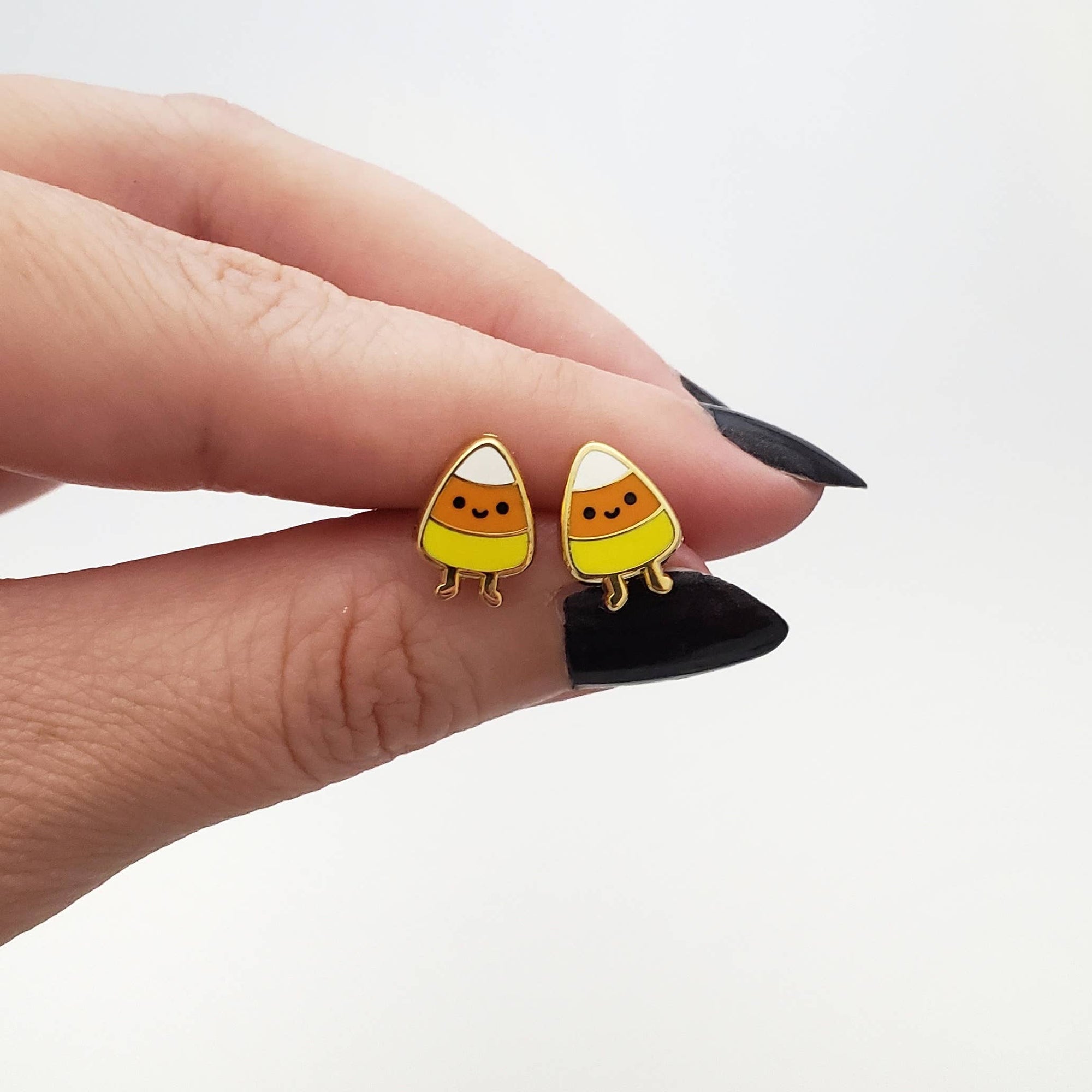Candy corn-shaped earrings held between fingers on a white background