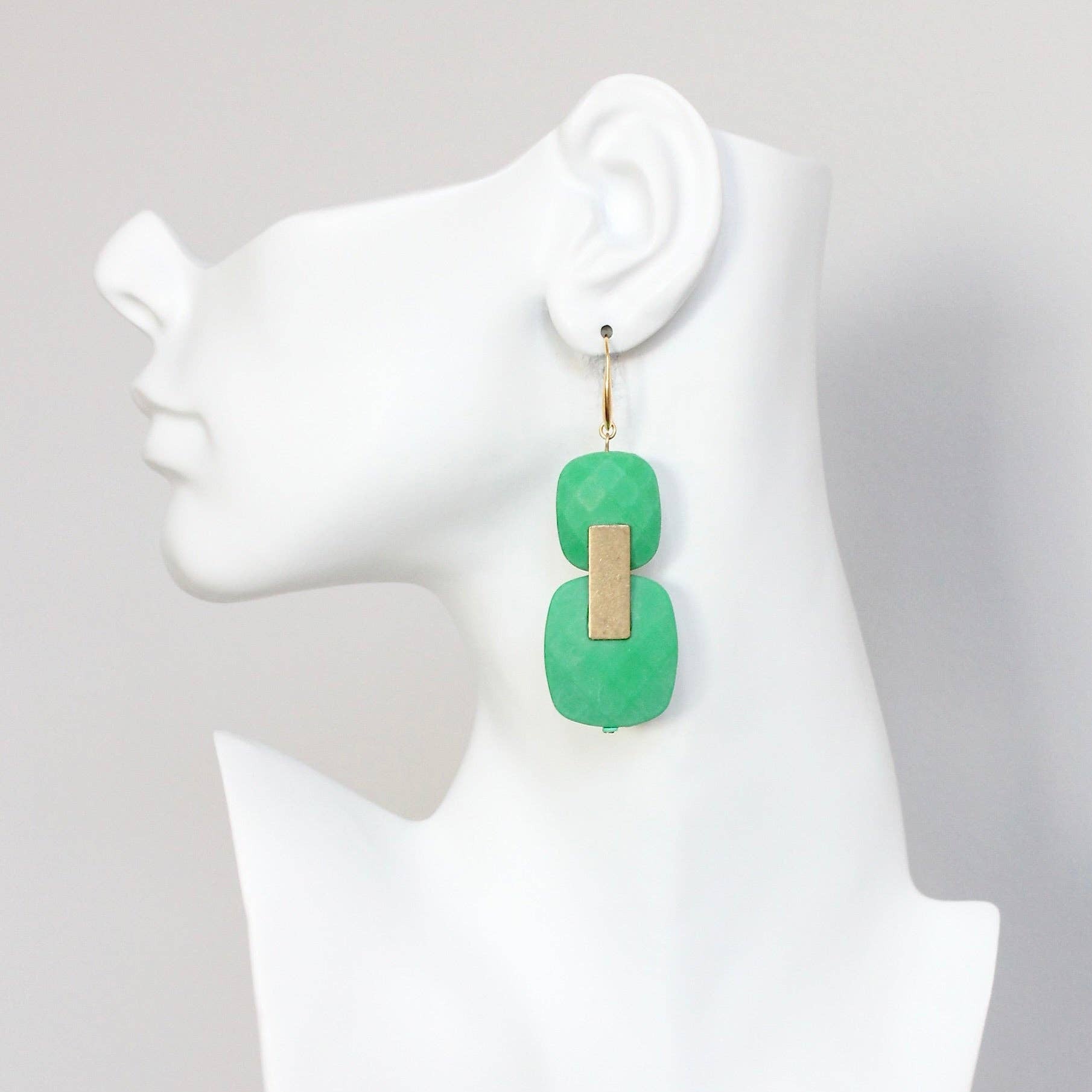 Green earrings on a mannequin ear with a plain background