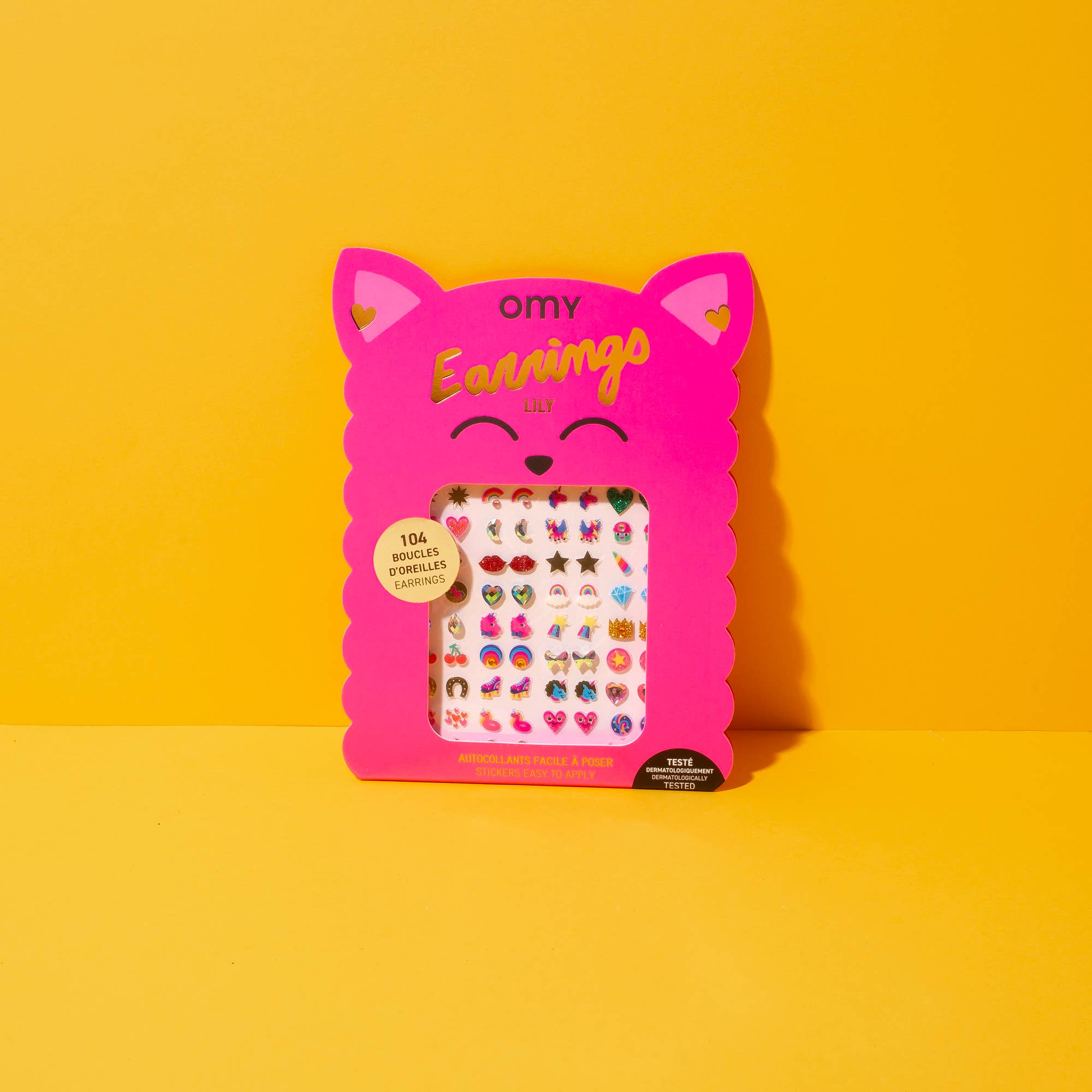 A box of stick-on earrings with various colorful designs presented in a pink box with a unicorn motif.