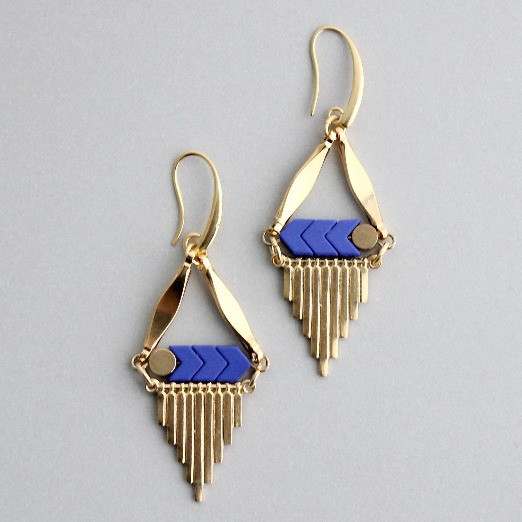Gold and blue geometric earrings on a gray background