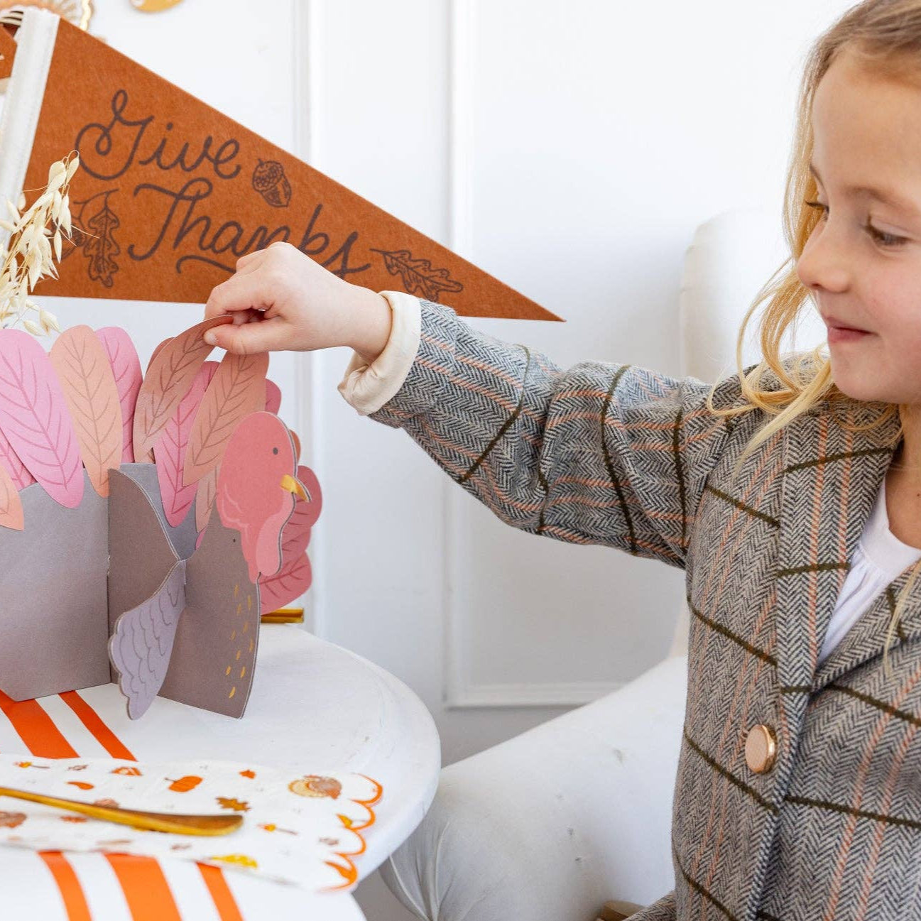 Child playing with a paper turkey decoration at a Thanksgiving-themed table.