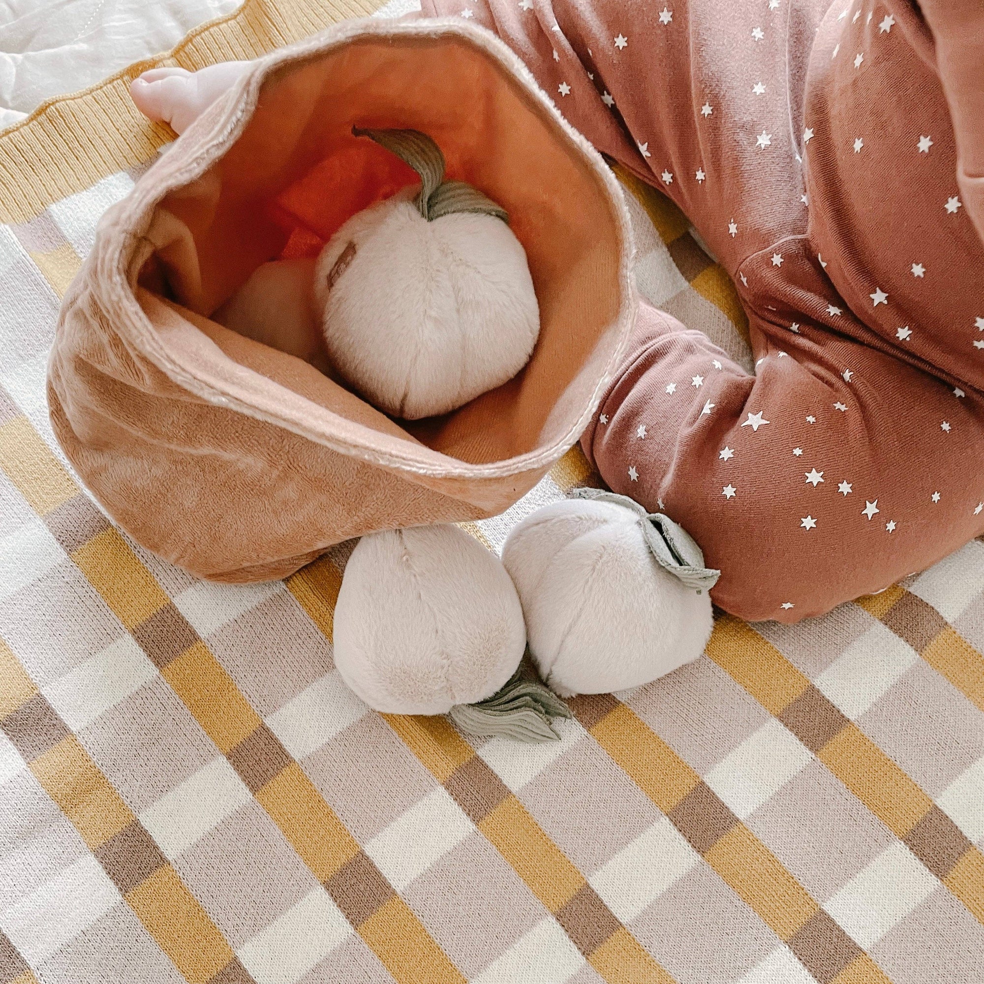 White plush pumpkins in a brown fabric bag on a checkered fabric background