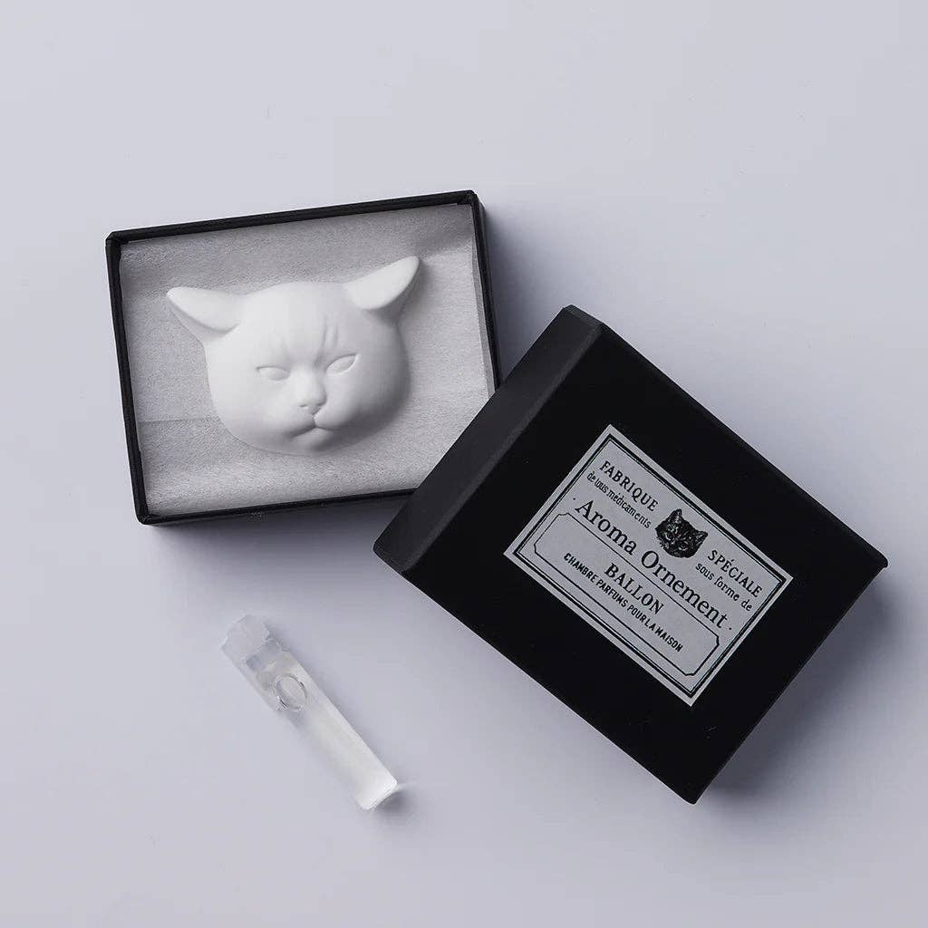 Cat-shaped ceramic in a black box with a label on a light gray background. Bottle of diffuser oil as well.