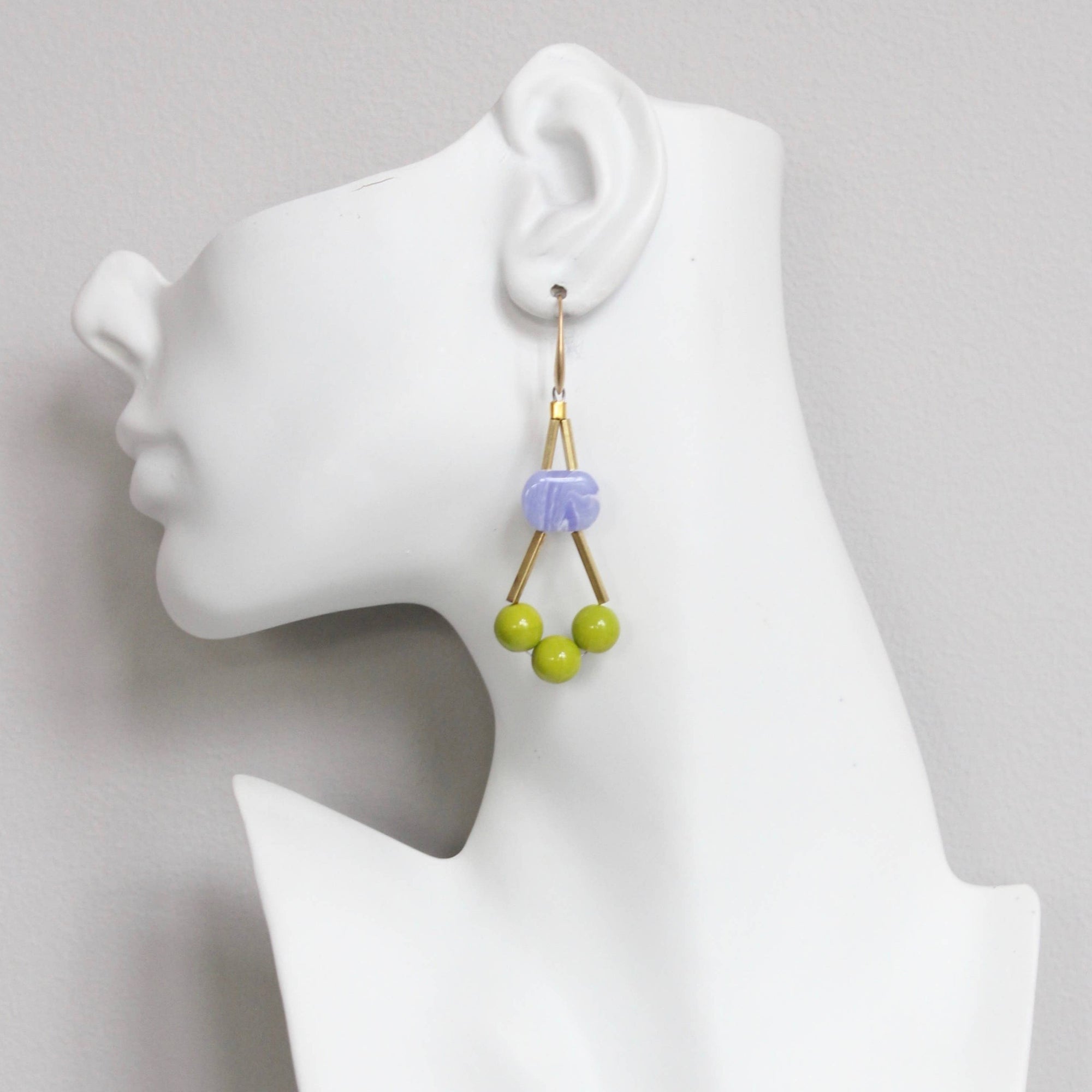 Earrings with green beads on a mannequin ear against a gray background