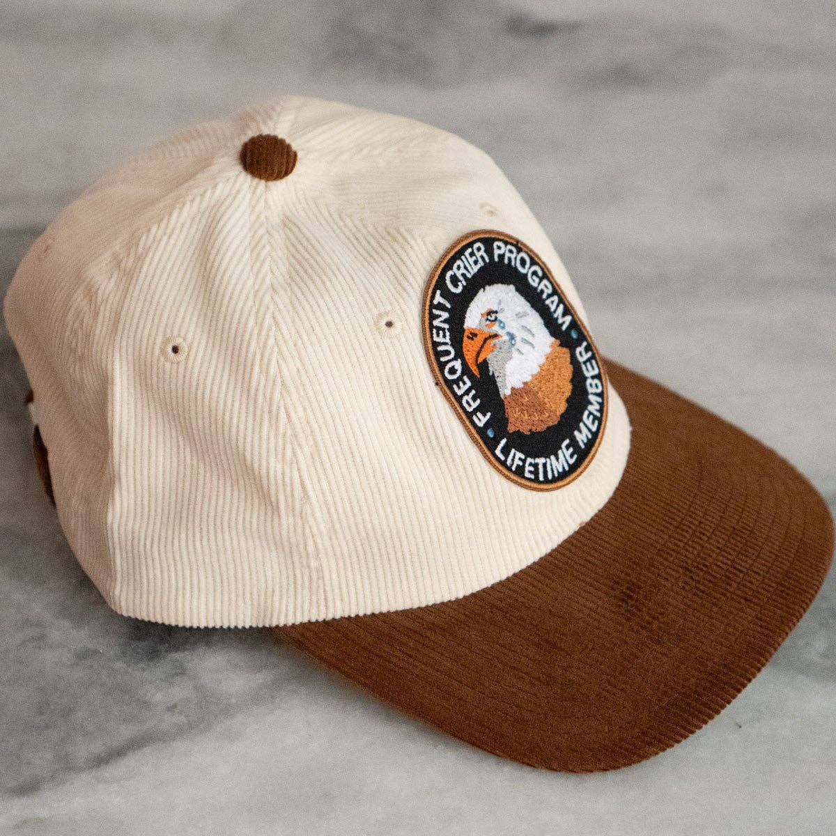 Beige and brown cap with an eagle emblem on a gray surface