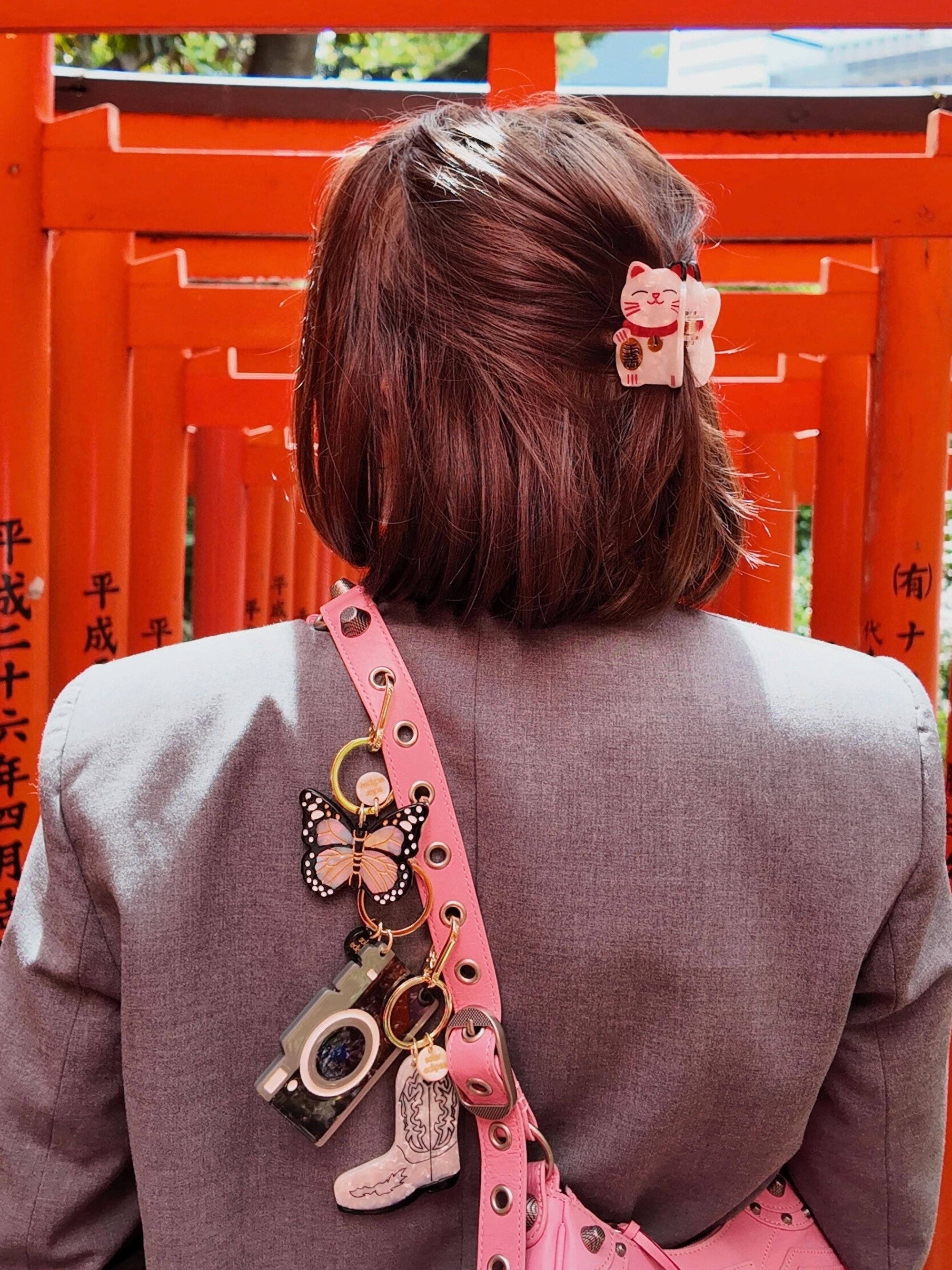 Person with pink hair clip and pink bag with charms against a red torii gate background