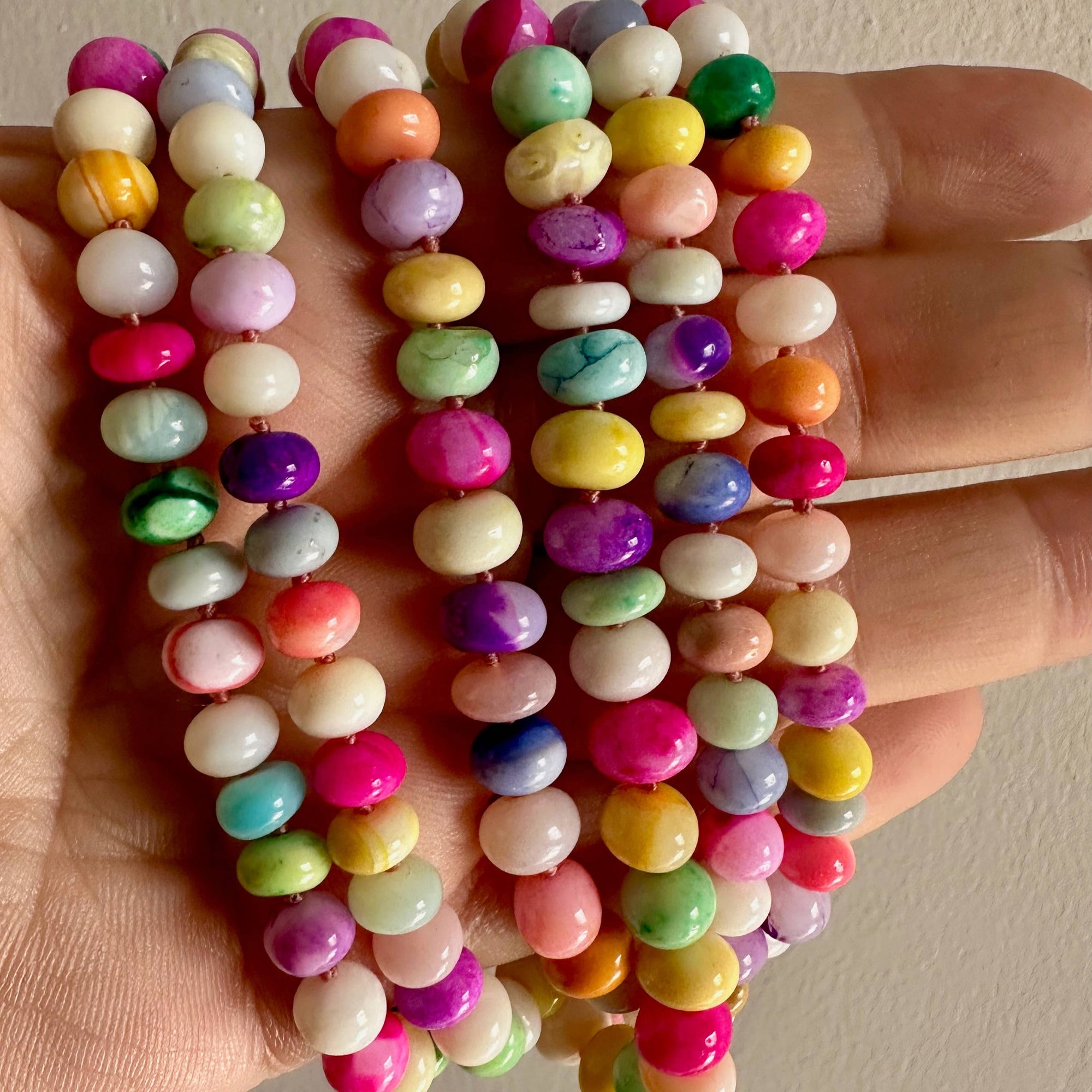 Colorful beaded bracelets held in a hand against a neutral background