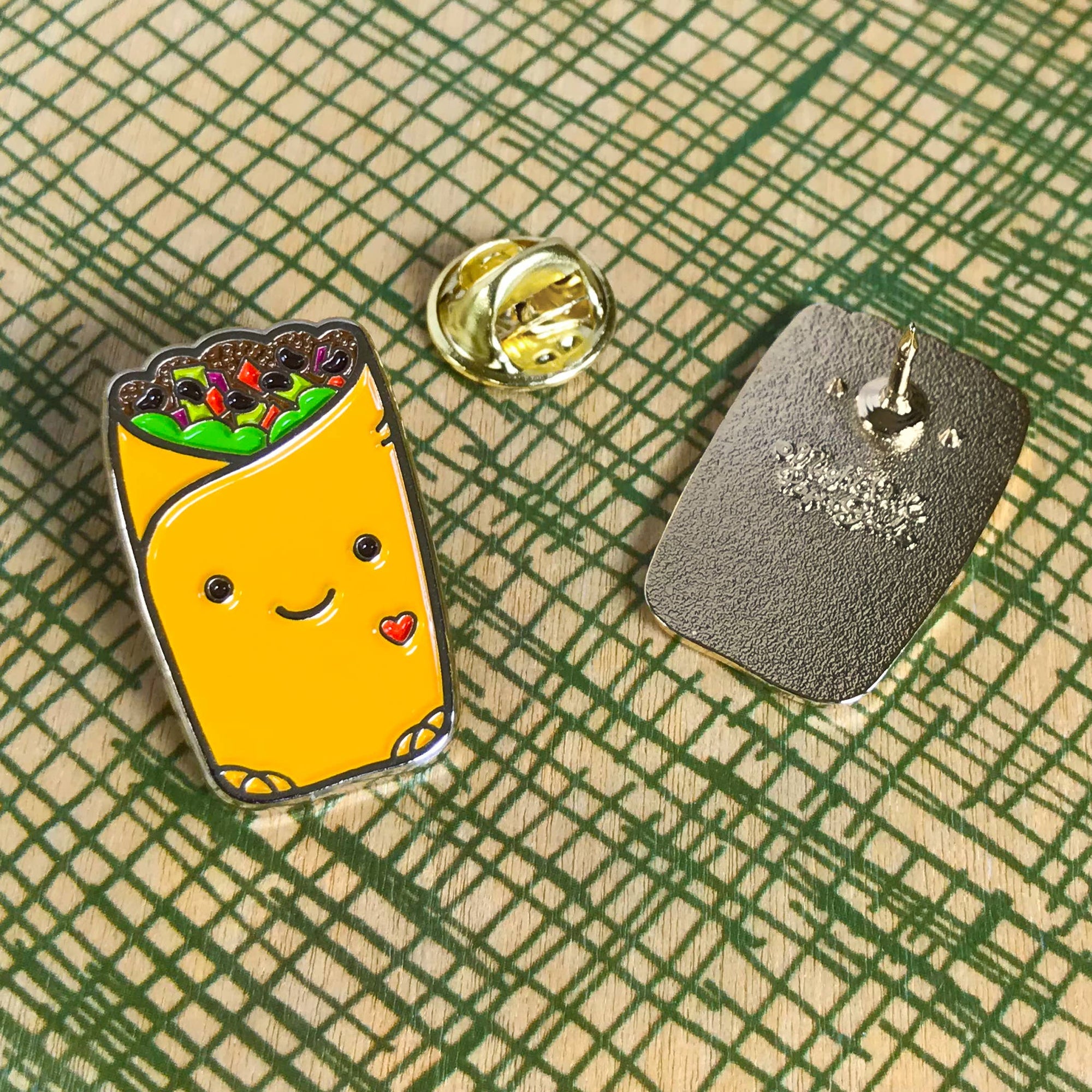 Enamel pin of a smiling burrito with a happy face on a textured surface