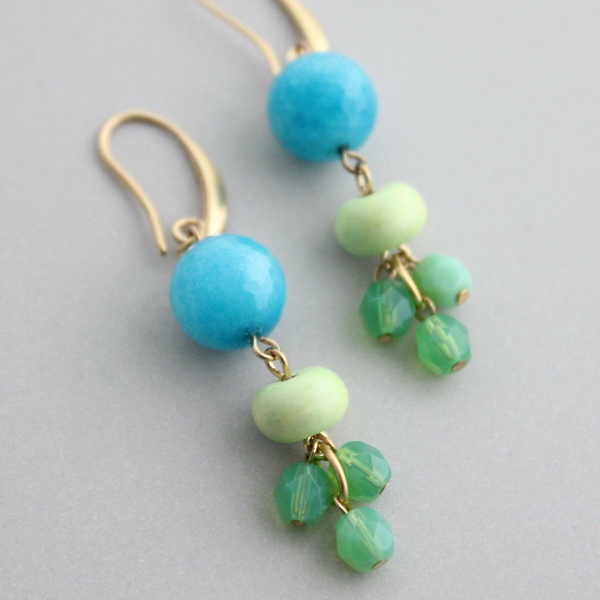 Pair of earrings with turquoise and green beads on a gray background