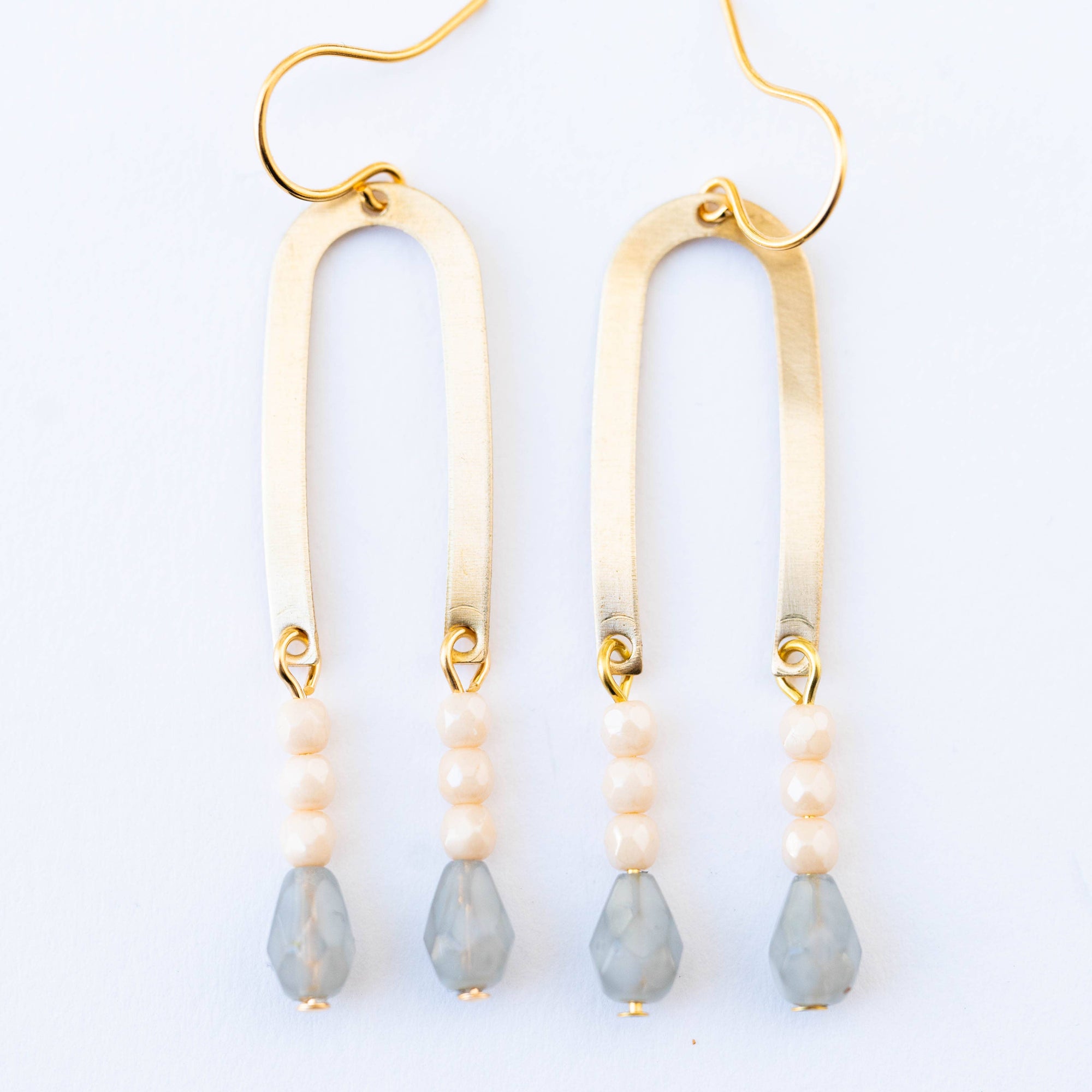 Gold earrings with beige and gray beads on a white background