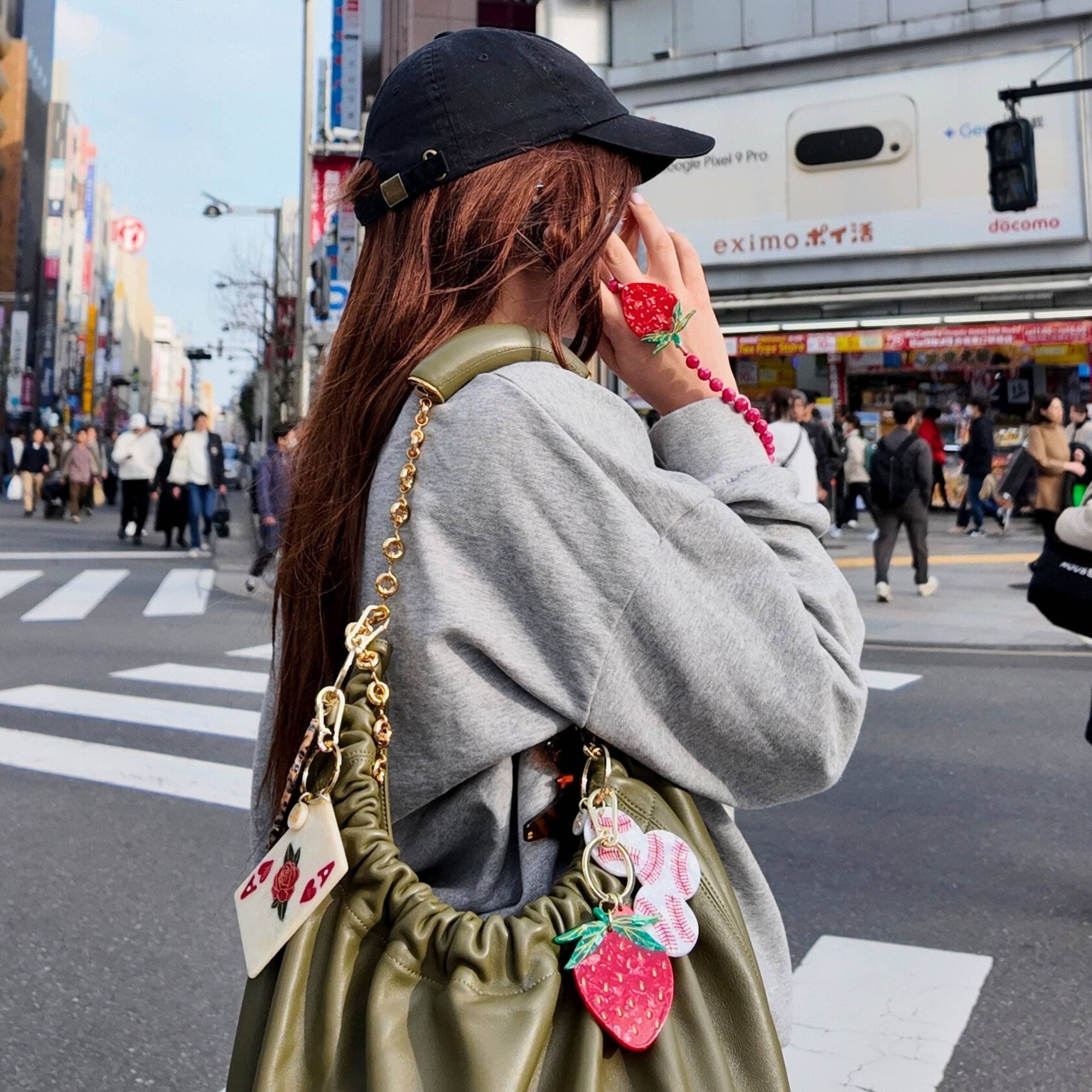 Woman in a city street wearing a green bag with strawberry charms