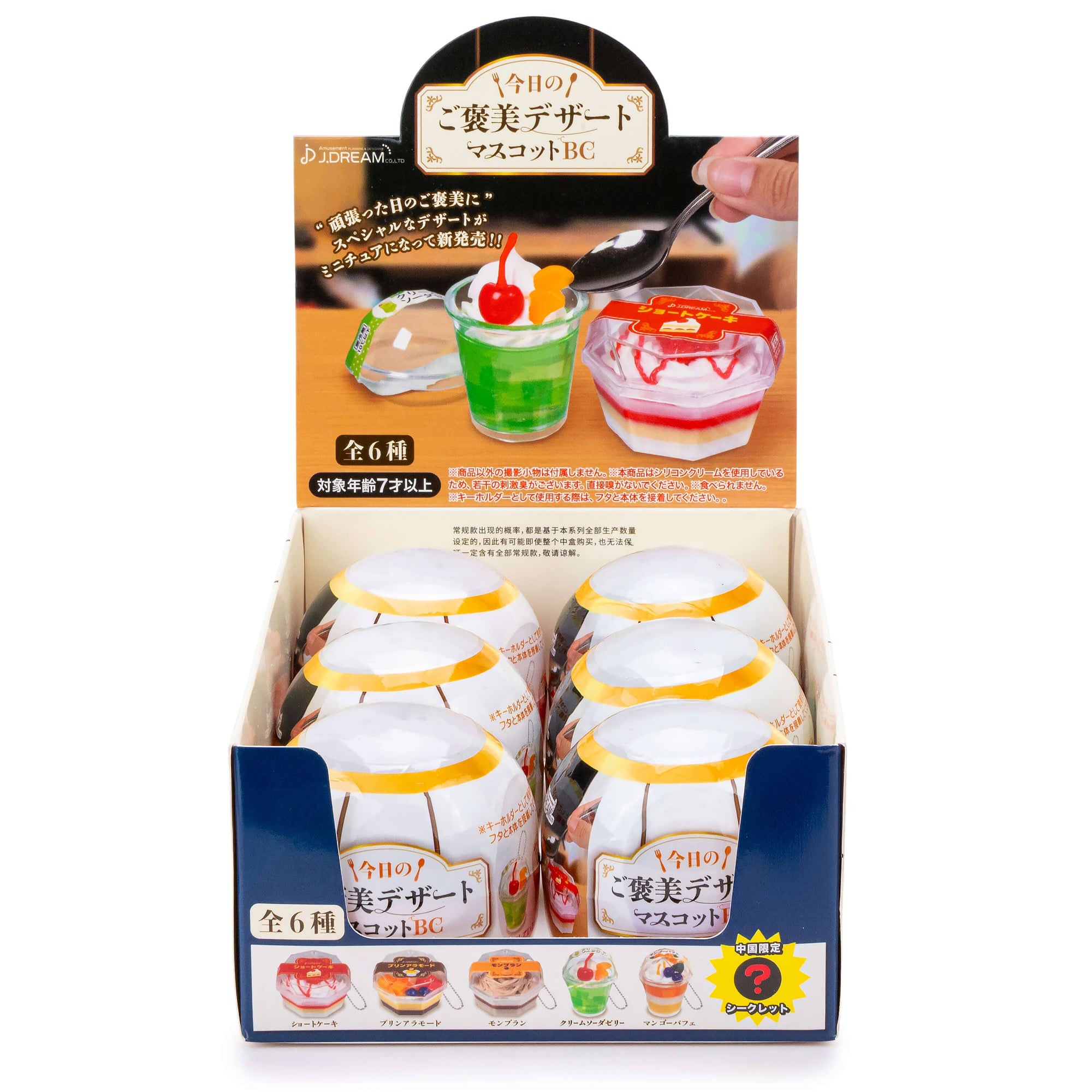 Display box of dessert figurines with colorful toppings and a spoon.