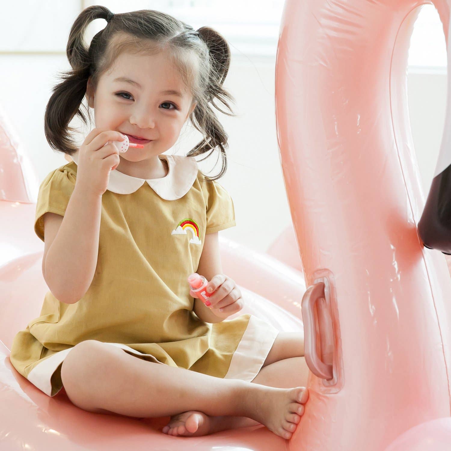 Child in a yellow dress sitting on a pink inflatable chair.