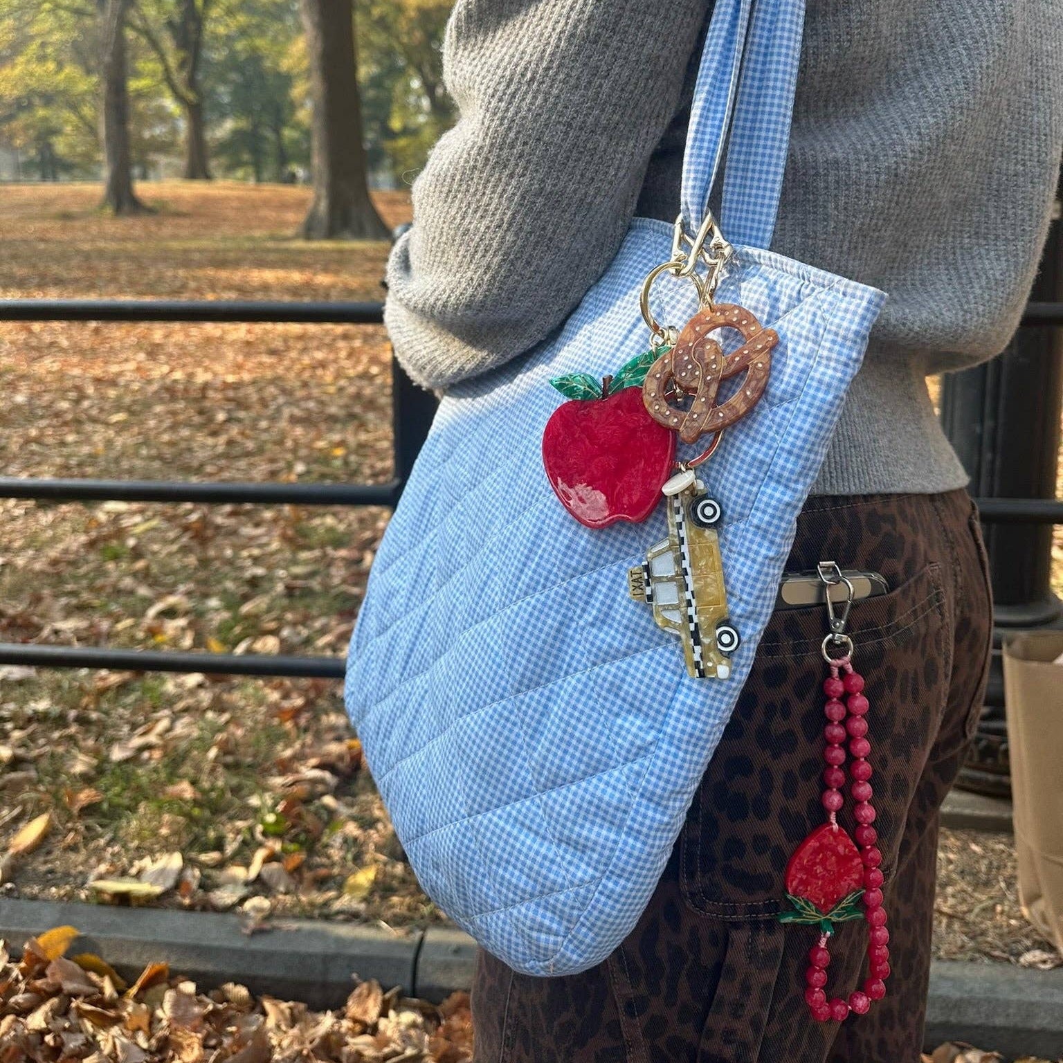 Person holding a blue quilted handbag with decorative elements in an outdoor setting