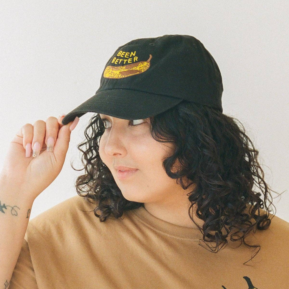 Person wearing a black cap and tan t-shirt with a banana graphic and 'BeeN Better' text.
