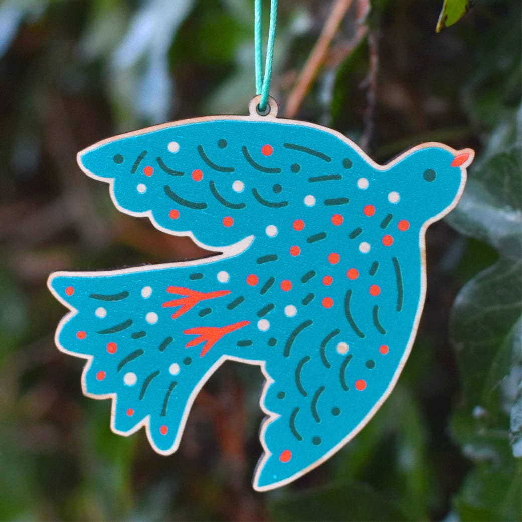 Decorative blue dove ornament with red and white patterns hanging against a green leafy background