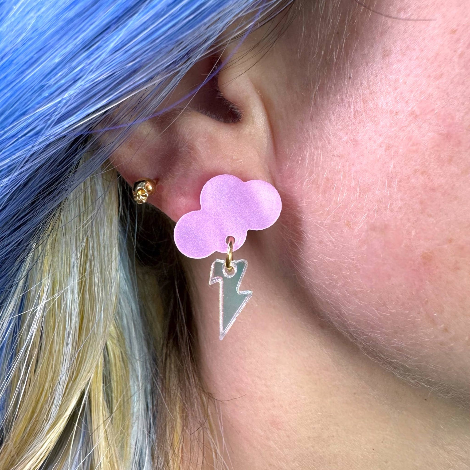 Close-up of an ear wearing a purple cloud-shaped earring with a green lightning bolt charm.