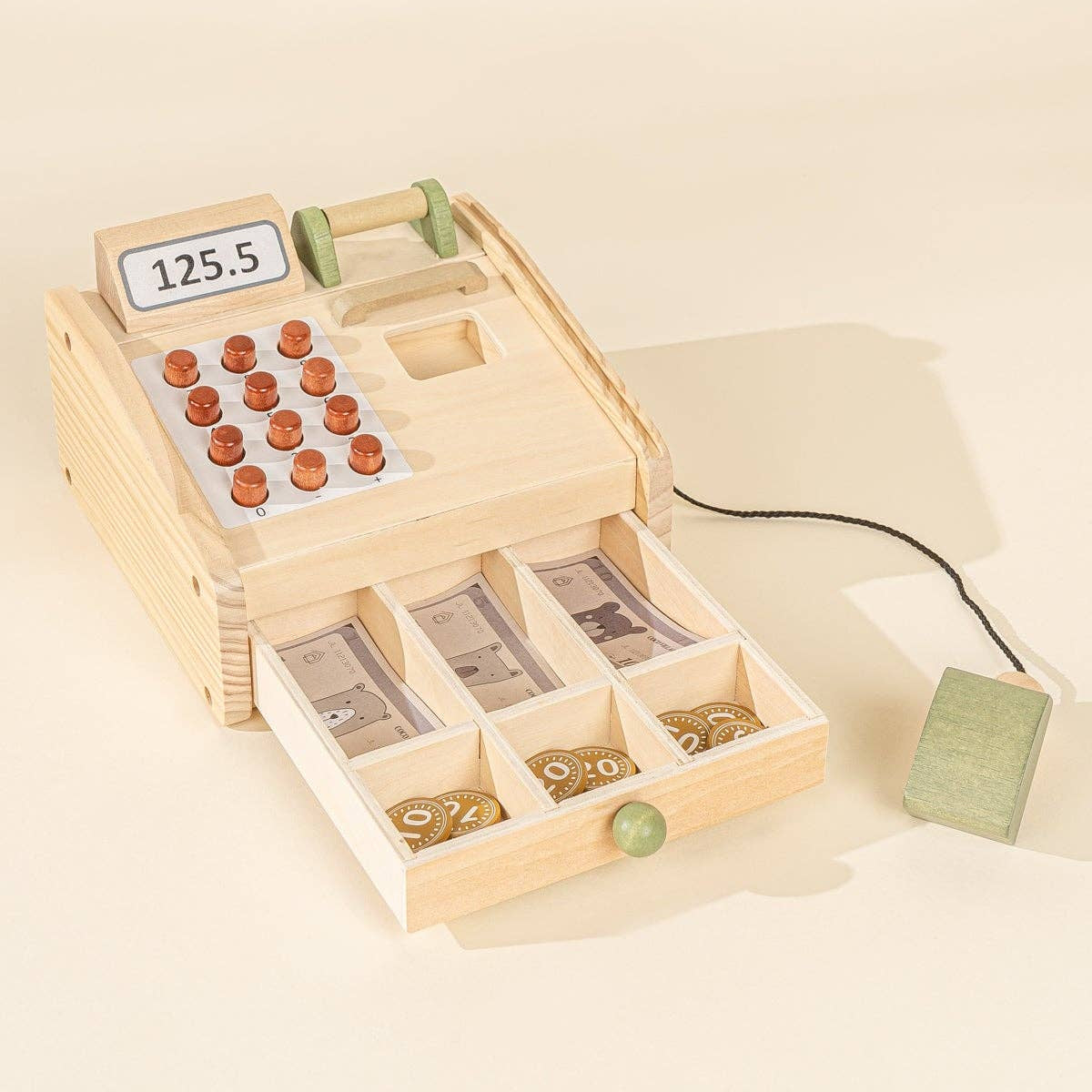Wooden toy cash register with coin compartment on a beige background