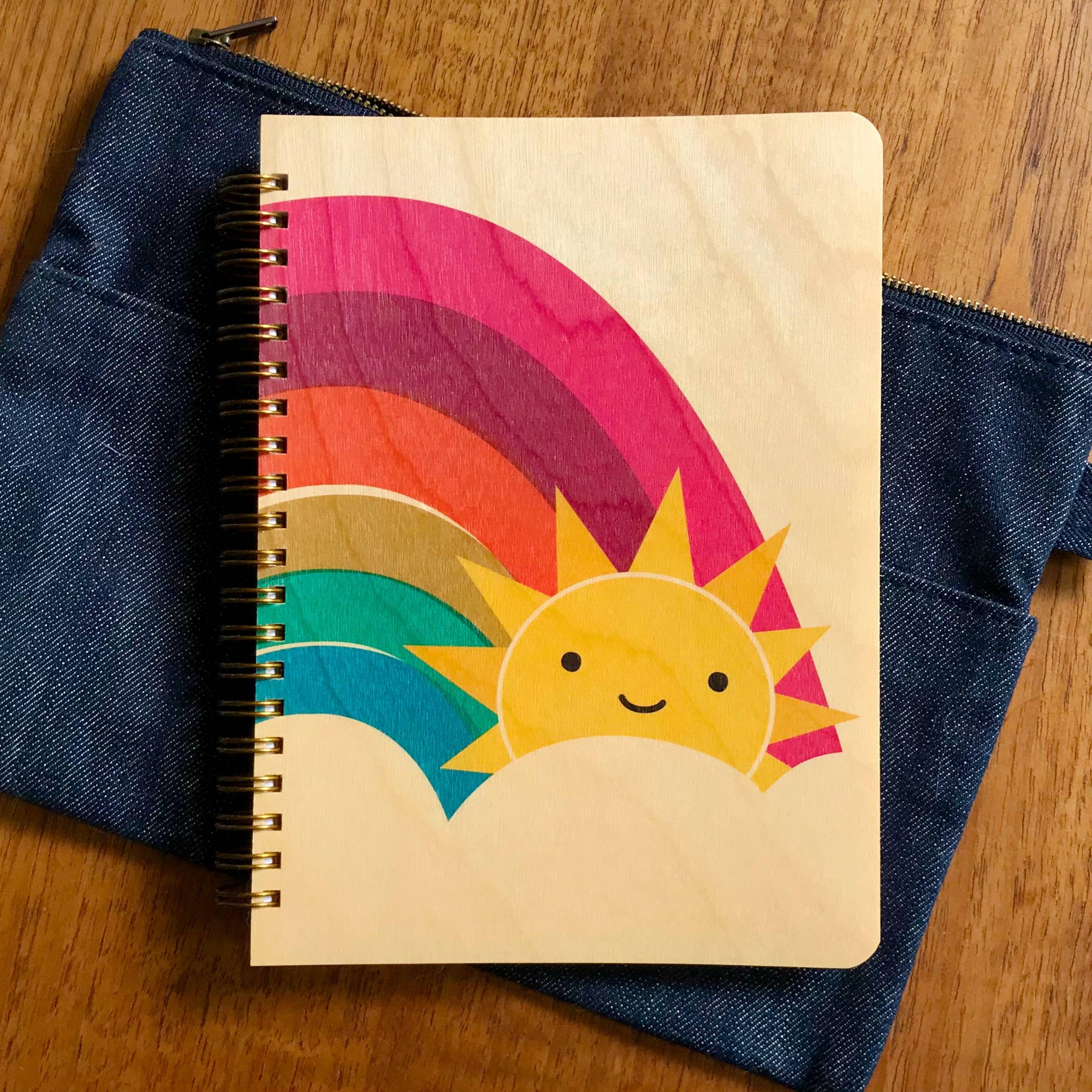 Notebook with a colorful rainbow and sun design on a denim surface.