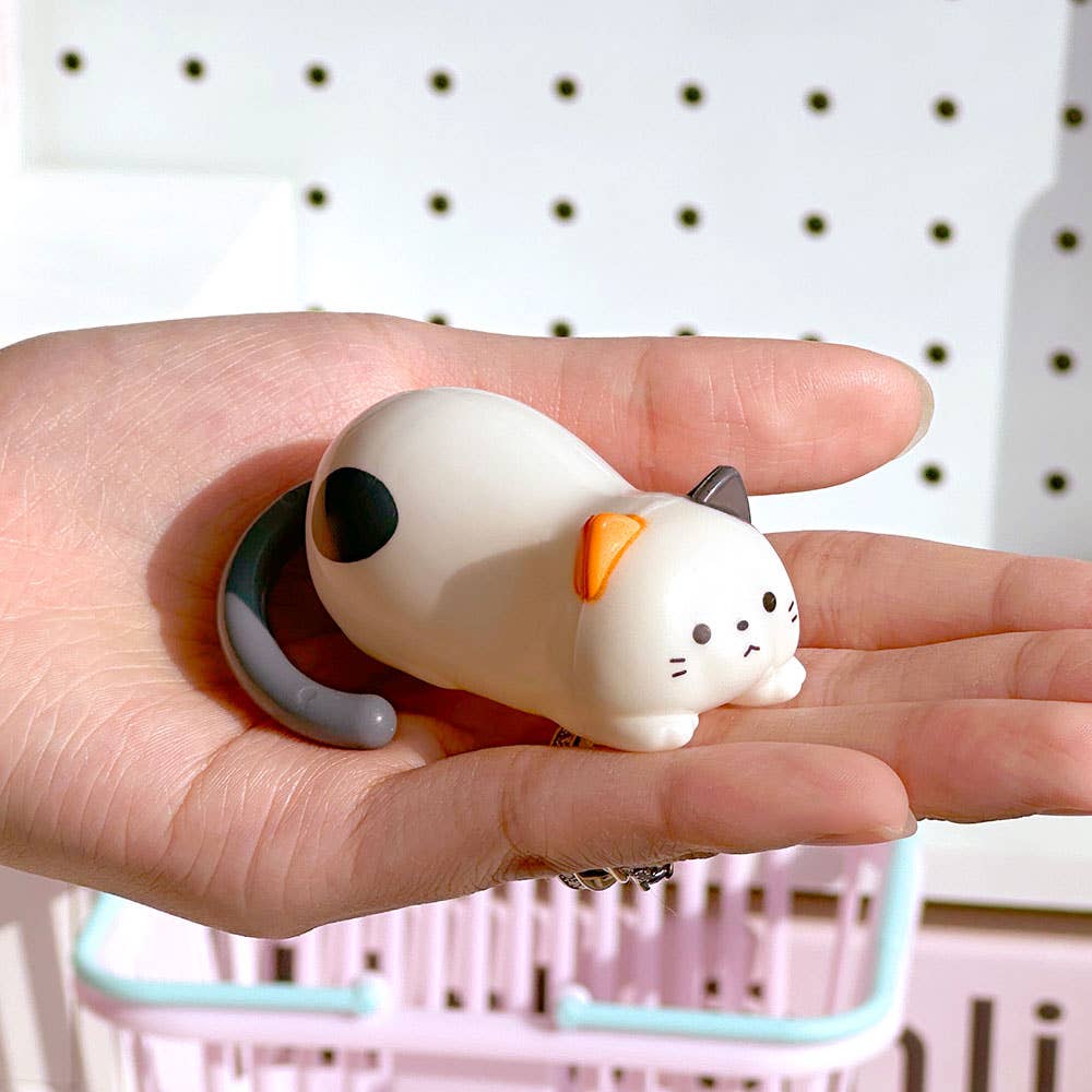 Small white cat figurine held in a hand with a blurred background