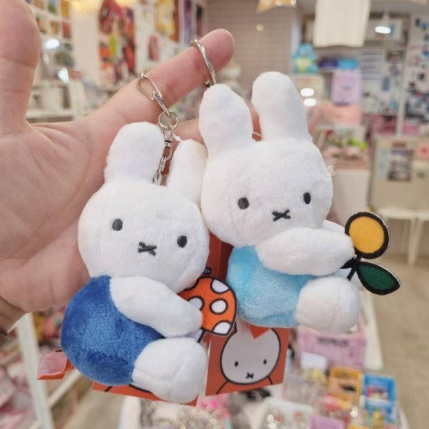 Two plush rabbit keychains held by a hand with a blurred store background.