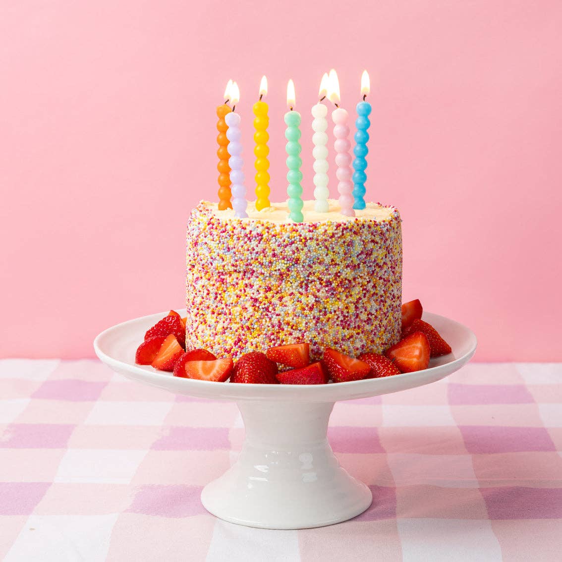 Birthday cake with colorful candles and sprinkles on a pink background