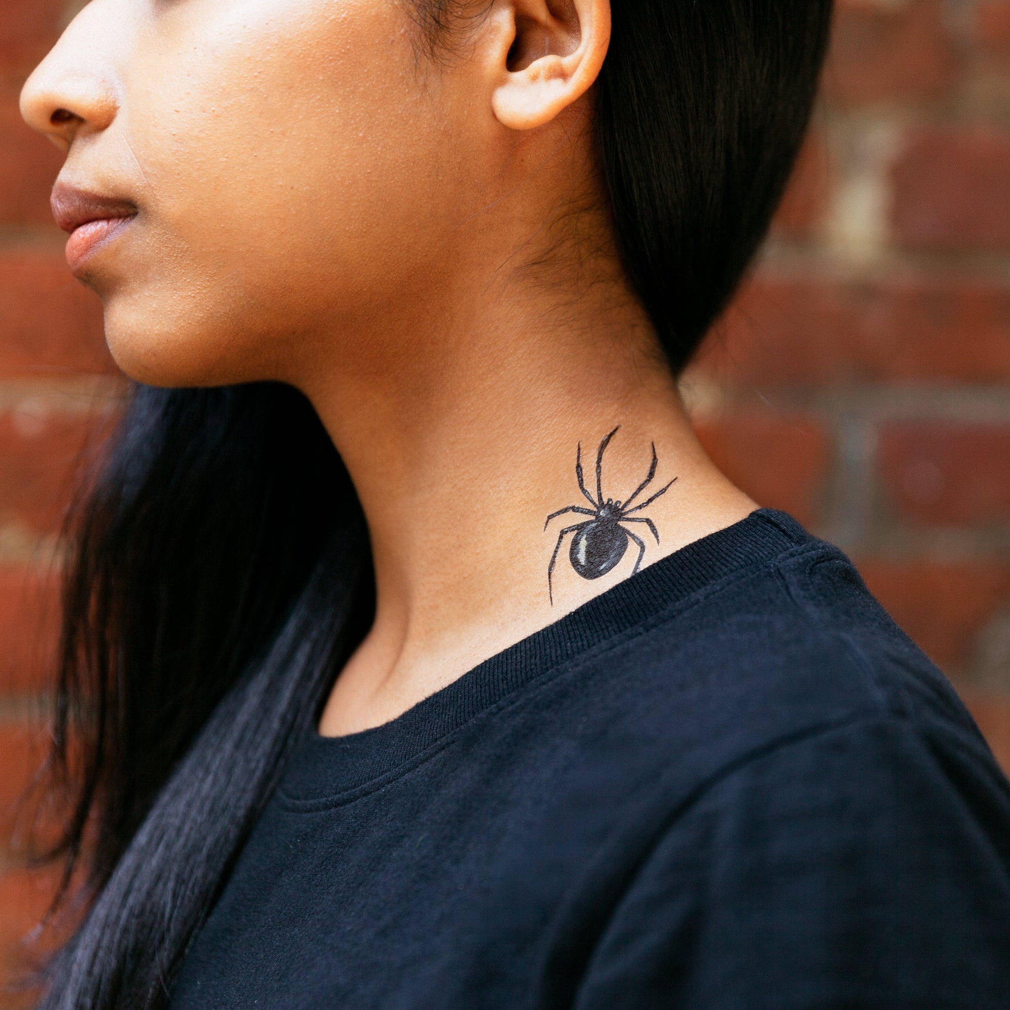 Person with a spider tattoo on their neck against a brick wall.