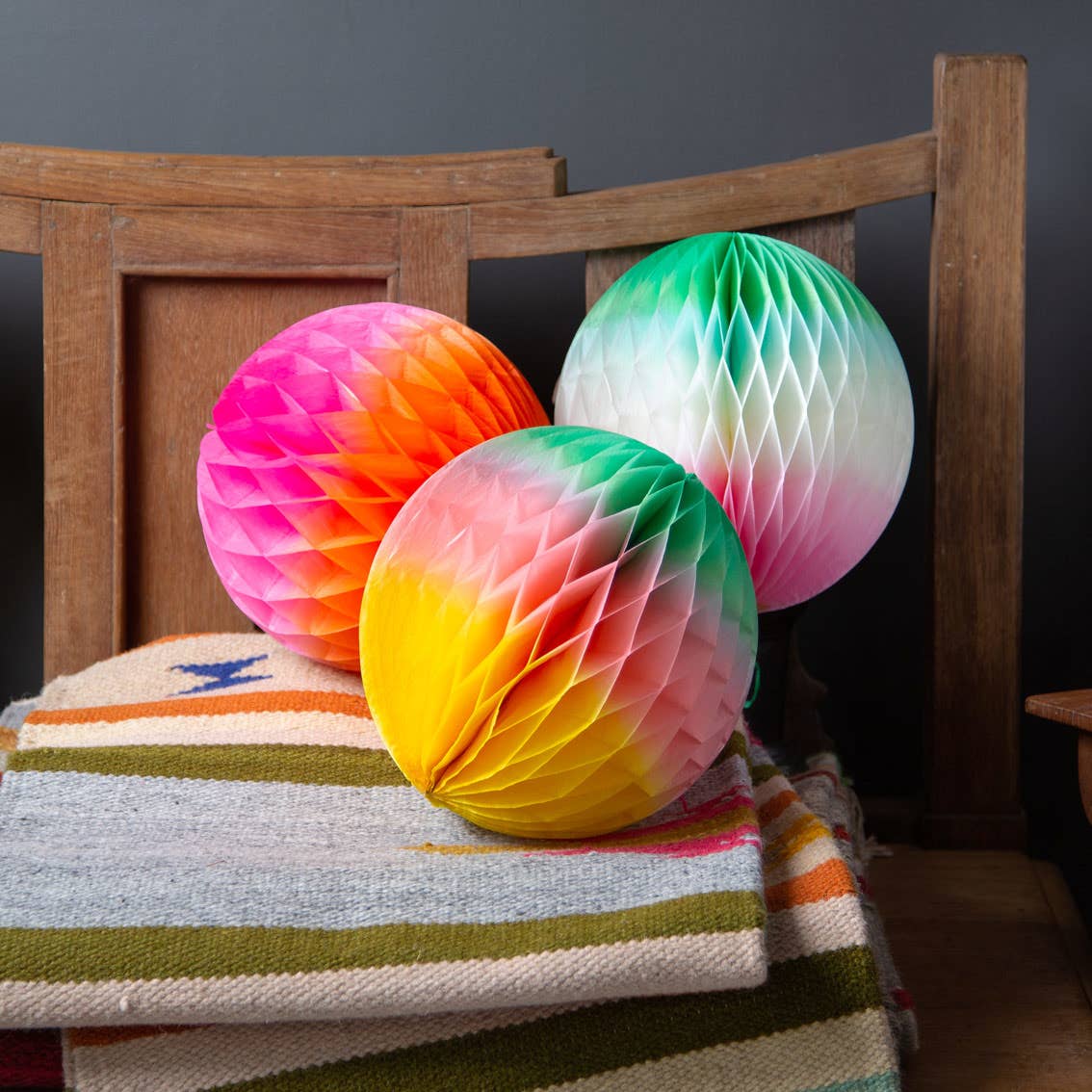 Colorful honeycomb balls on a striped blanket with a wooden chair in the background.