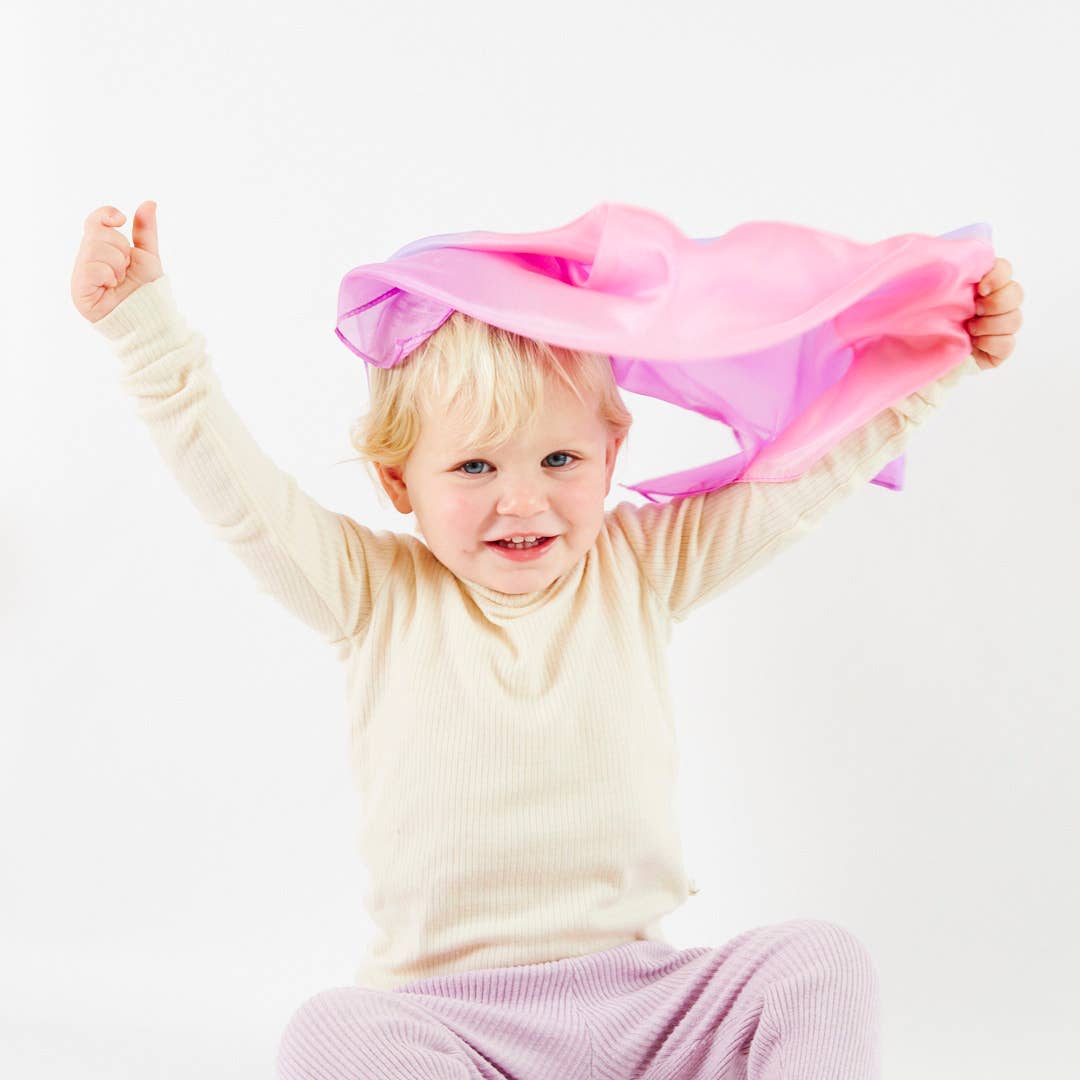 Child playing with a pink scarf on a white background