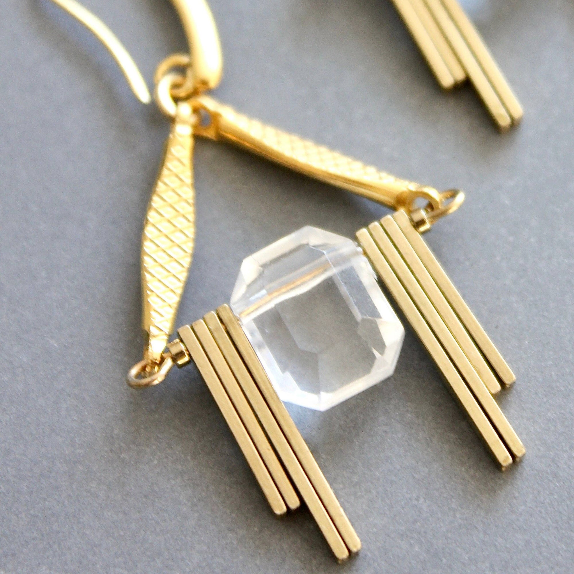 Gold earrings with clear gemstones on a gray background