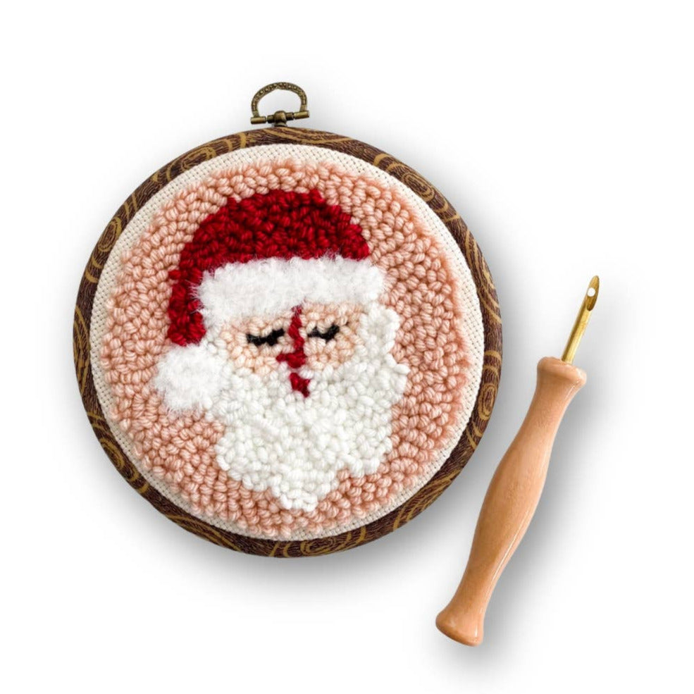 Embroidery hoop with a completed Santa Claus design and a wooden embroidery hook on a white background