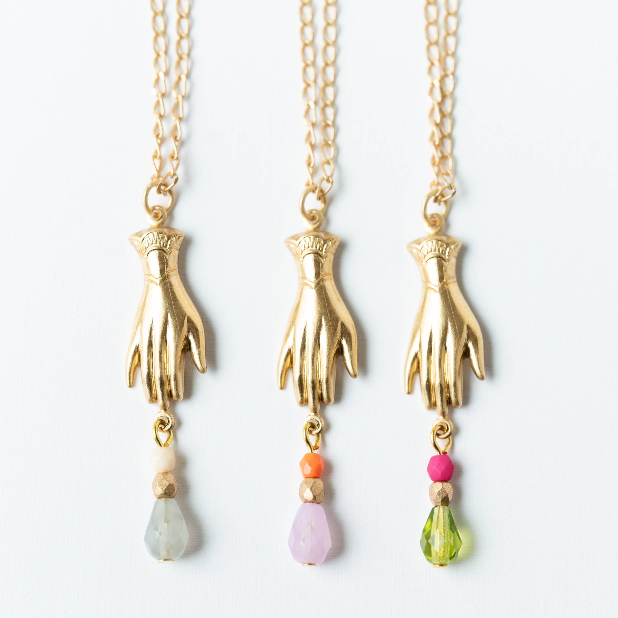 Three gold hand-shaped pendants with colorful beads on a white background