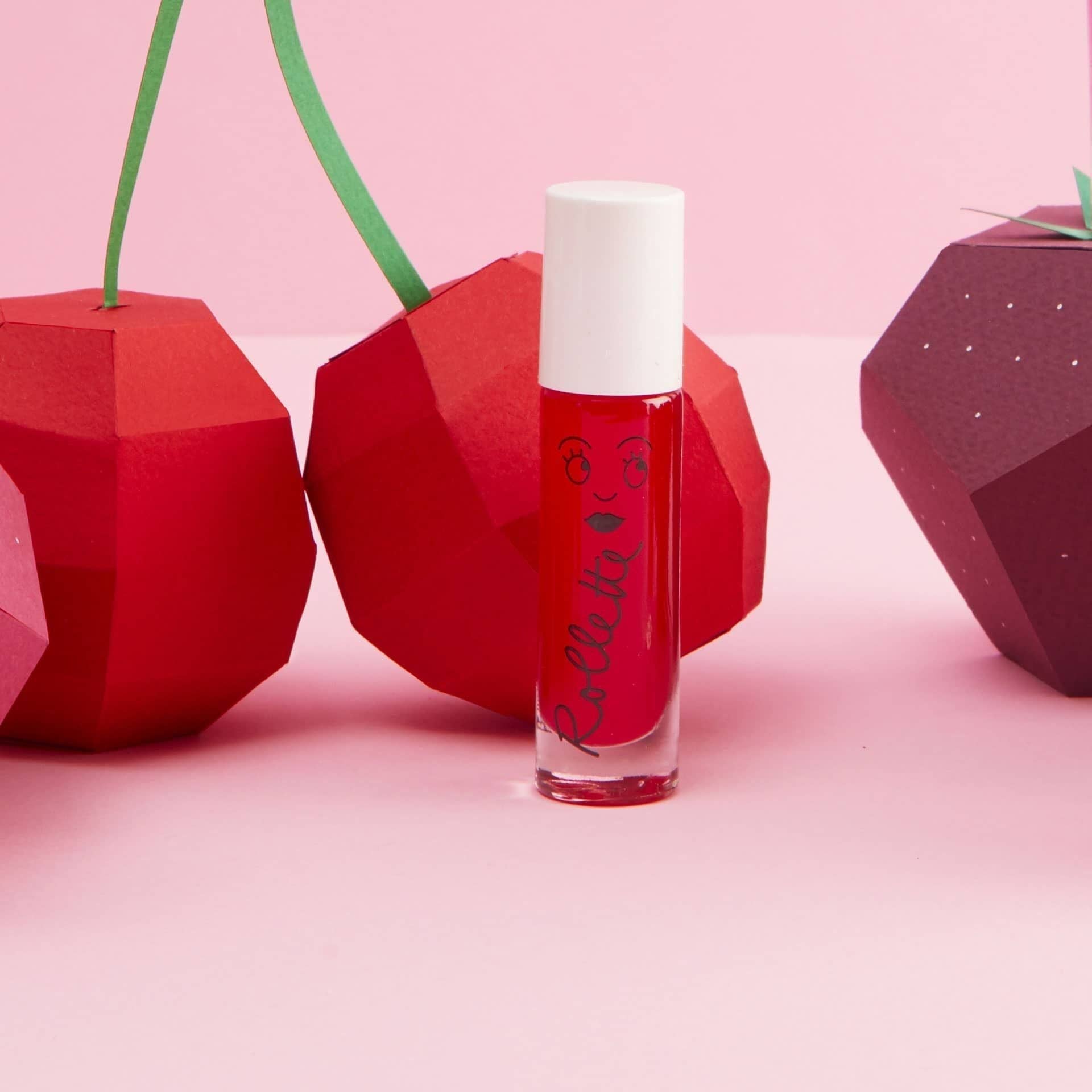 Red lip gloss bottle with white cap on a pink background with geometric cherry decorations