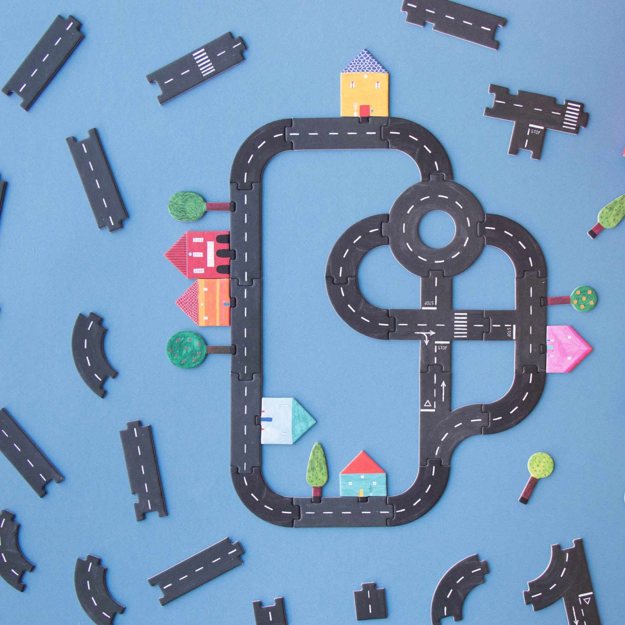 Toy road track set on a blue background with small buildings and trees.