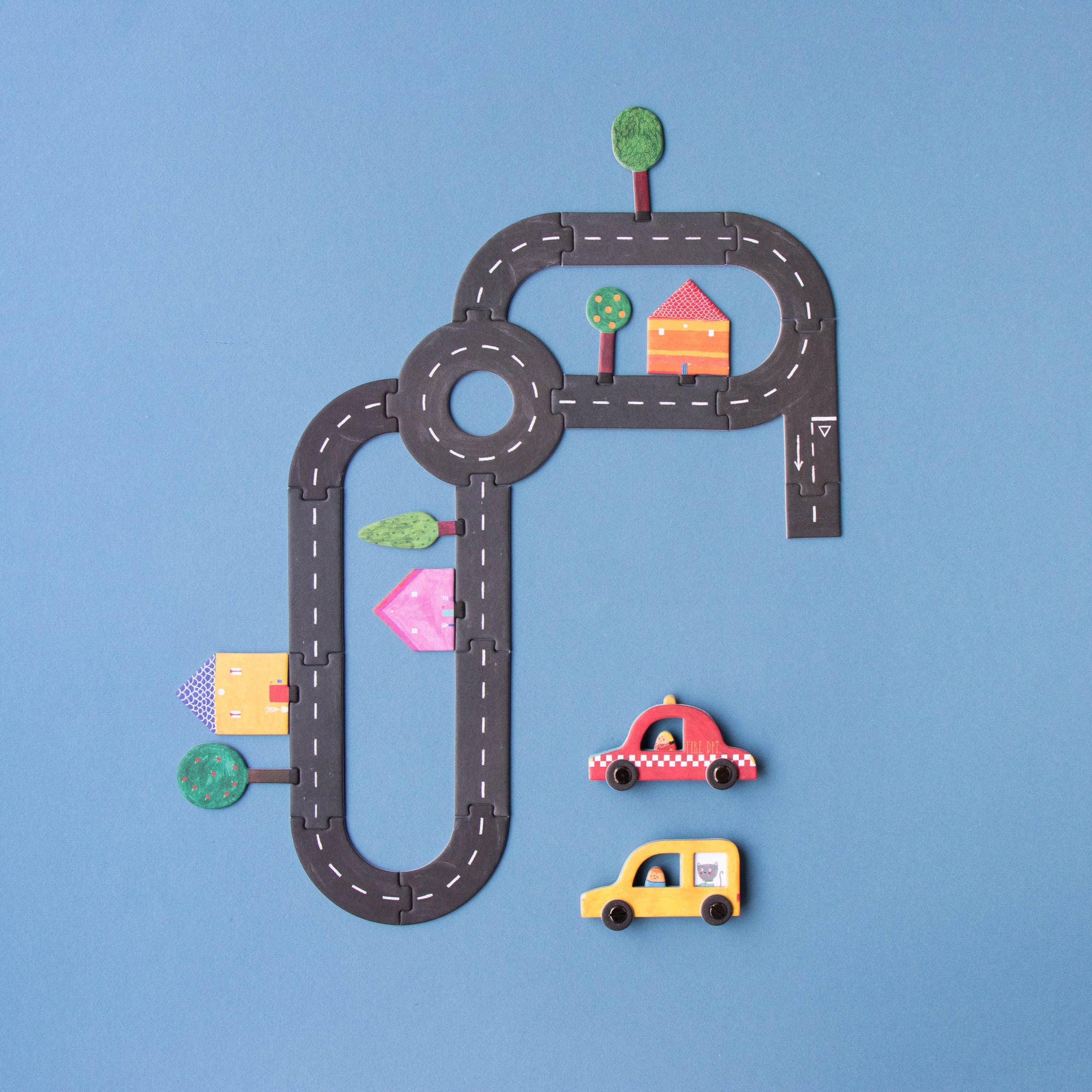 Toy cars on a paper road with small houses and trees on a blue background