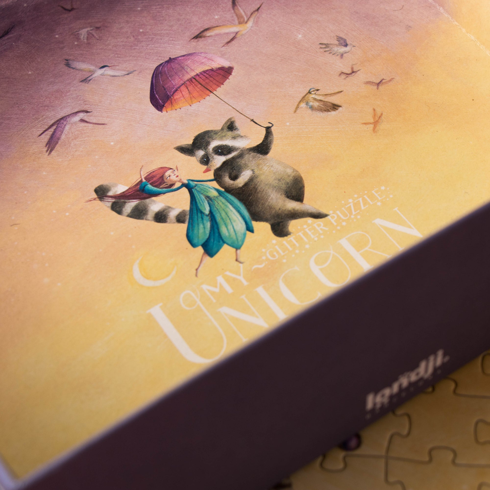 Jigsaw puzzle box with a raccoon and unicorn illustration on a gradient background