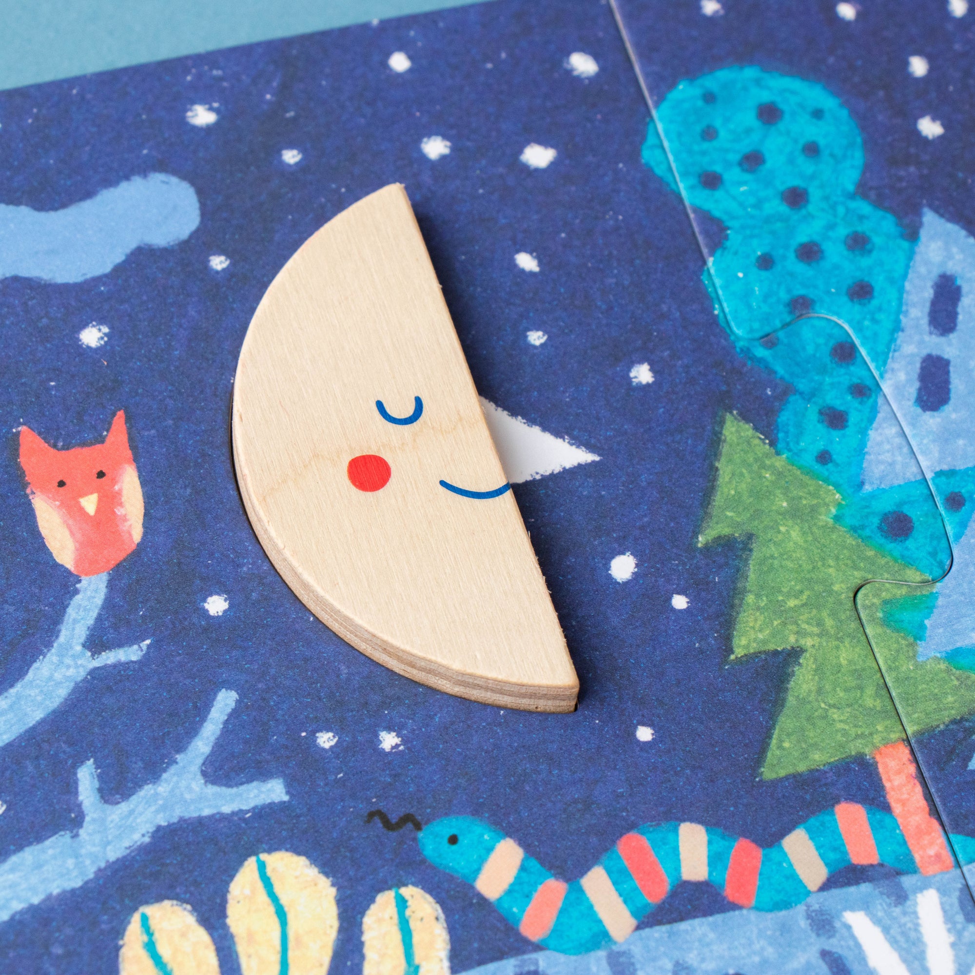 Wooden toy piece with a face on a blue snowy background with animal illustrations