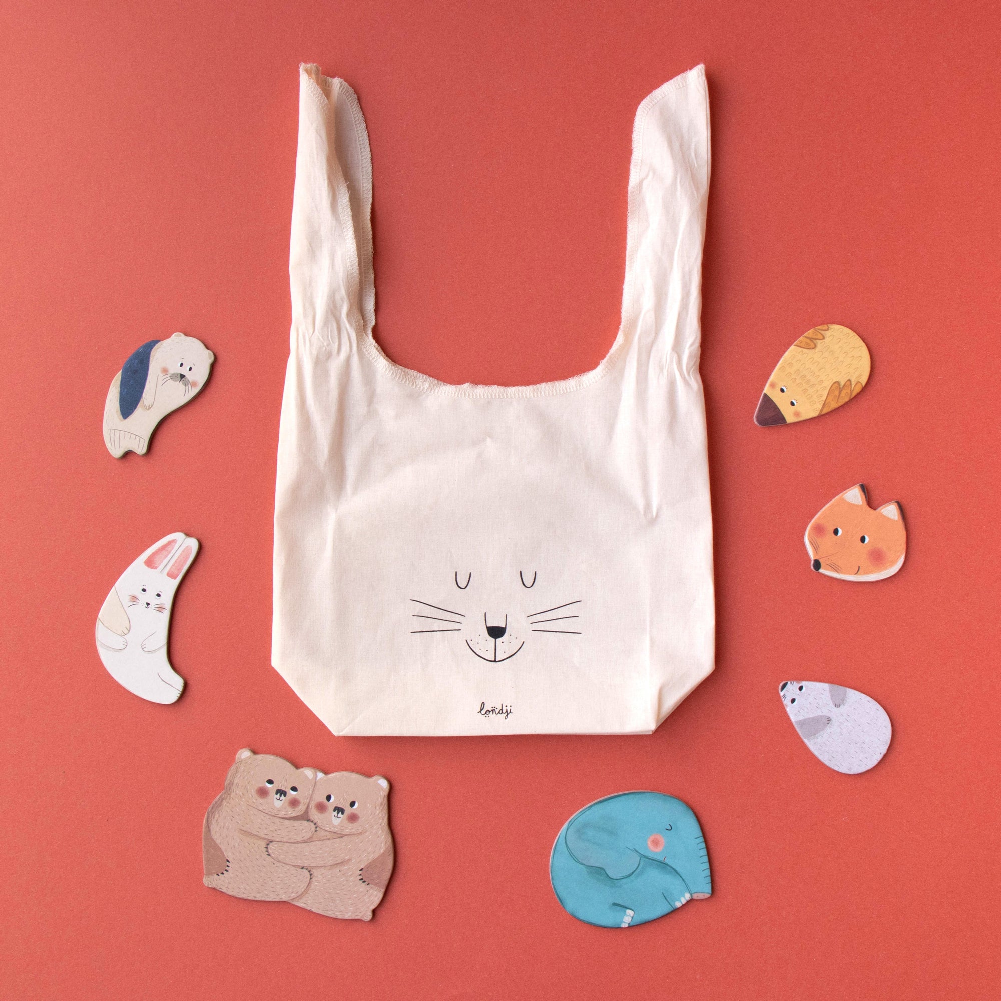 White reusable bag with bunny design surrounded by cartoon animal stickers on a red background