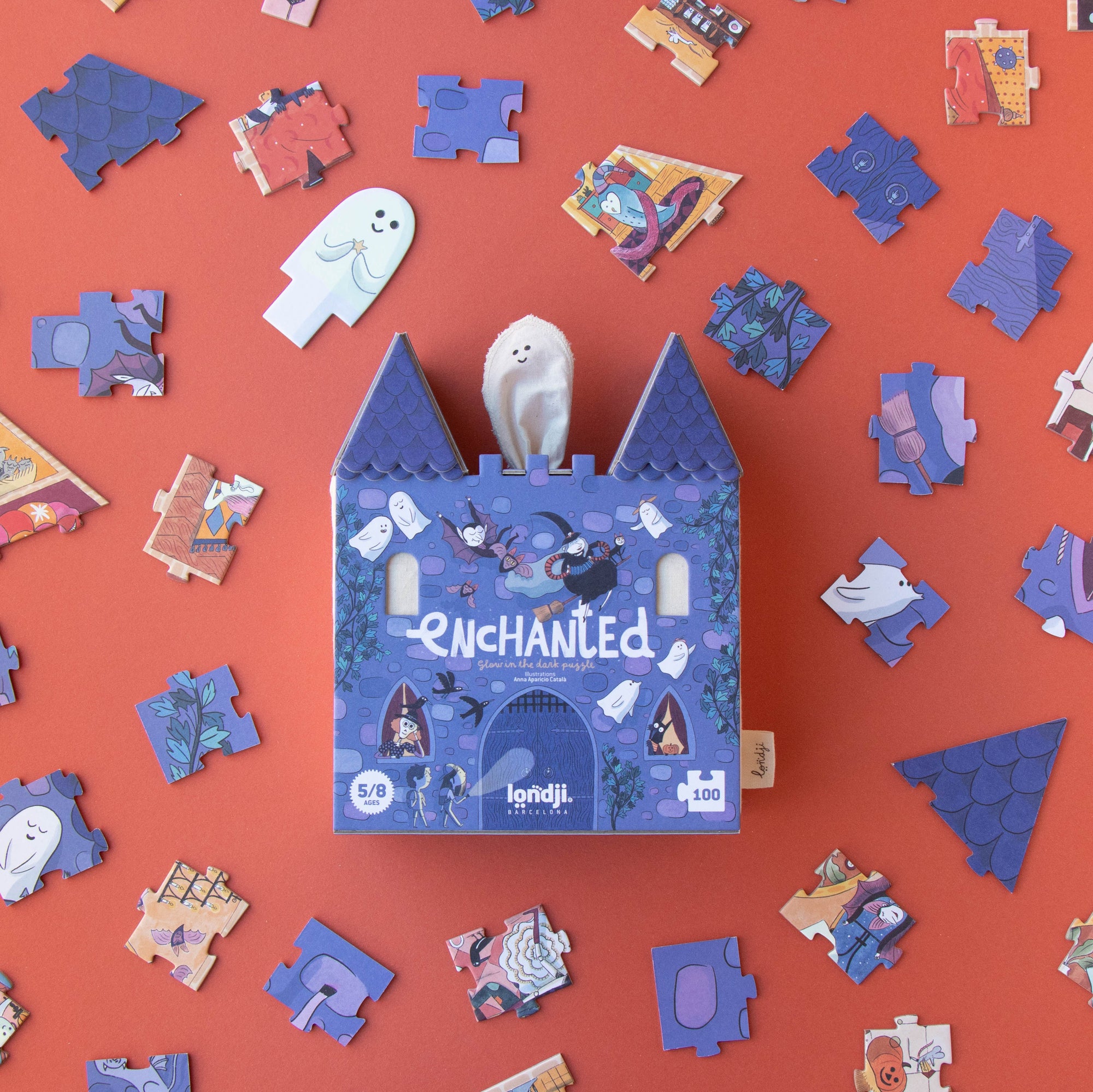 Blue castle-shaped puzzle box labeled 'Enchanted' surrounded by scattered puzzle pieces on a red background