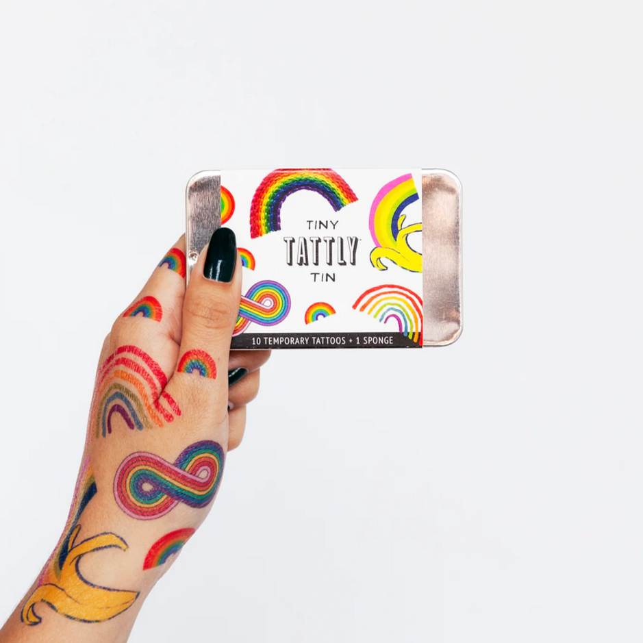 A hand holding a tin with colorful temporary tattoos, featuring a variety of rainbow patterns.
