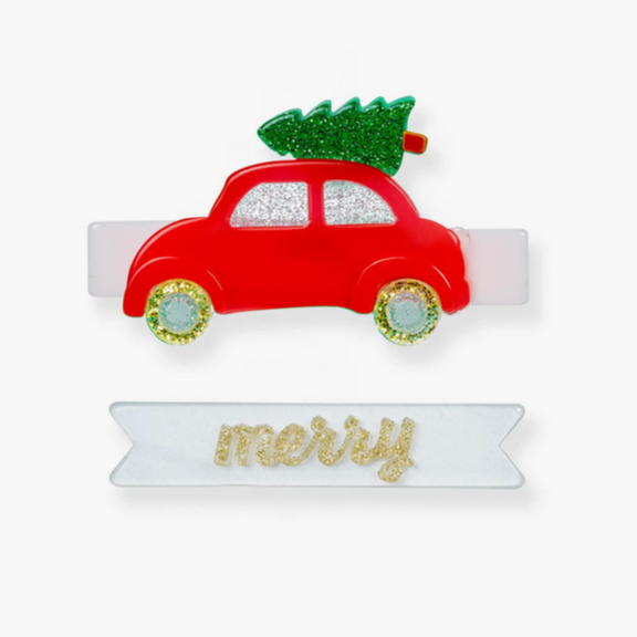 A red and green acrylic ornament in the shape of a car with a Christmas tree on the roof, attached to a white banner with the word 'merry' in a decorative font.