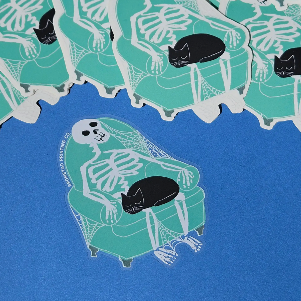 Clear stickers with a design of a cat resting on a skeleton, laid out on a blue surface.