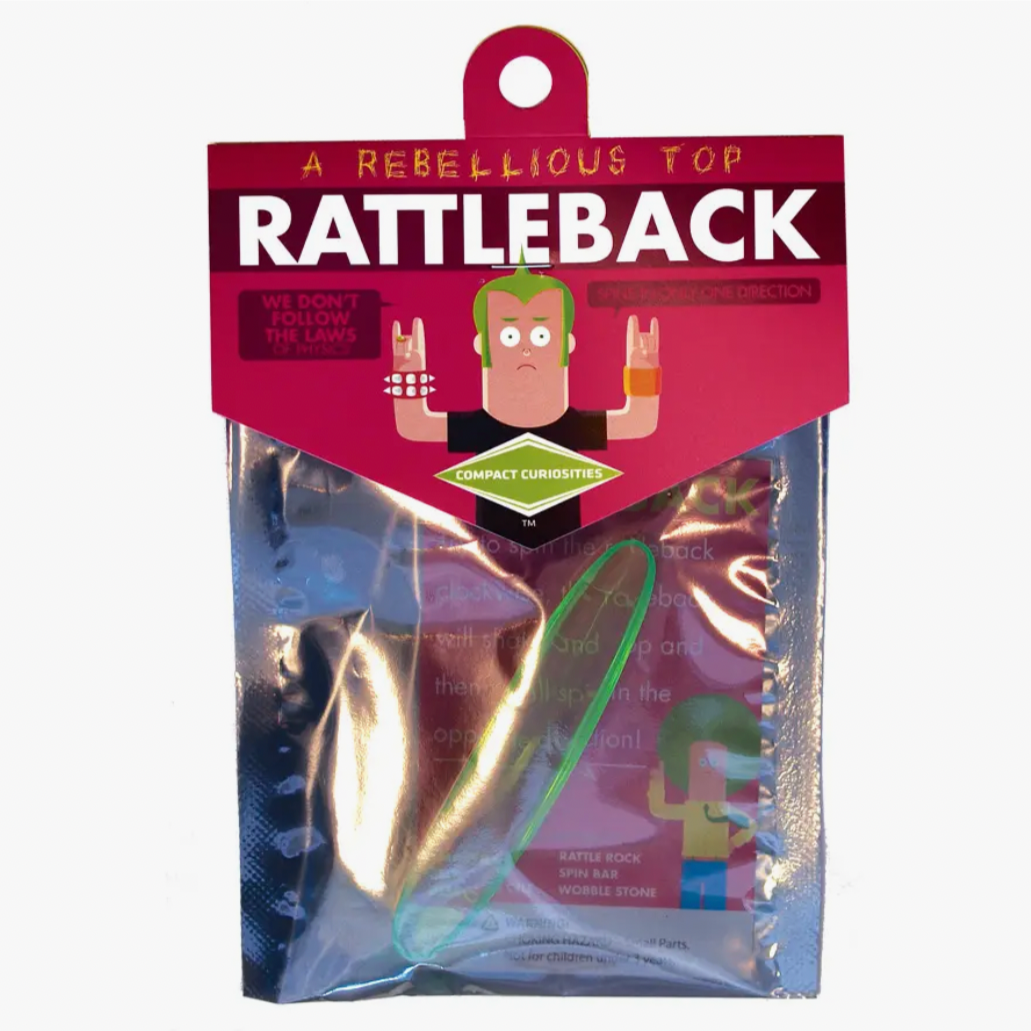 A packaged Rattleback toy with visible colorful design, displayed in front of a red and white product information label.