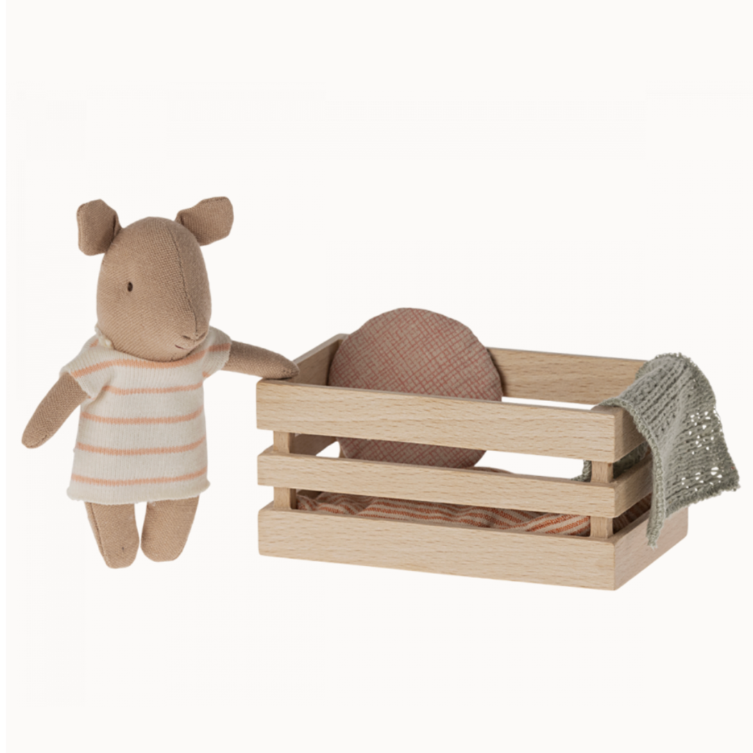 A toy pig in a wooden crate with a piece of soft bedding and a toy figure next to it.