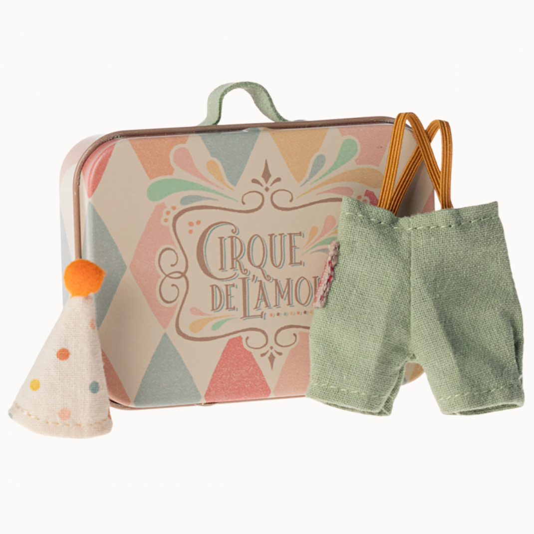 A small metal suitcase with a colorful circus-themed design, accompanied by a pair of green clown shorts and a party hat with an orange pom-pom.