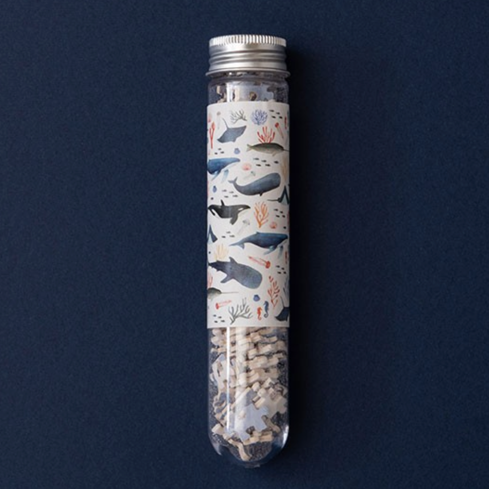 A cylindrical container with a clear top through which puzzle pieces and an illustration of sea animals are visible, against a dark background.